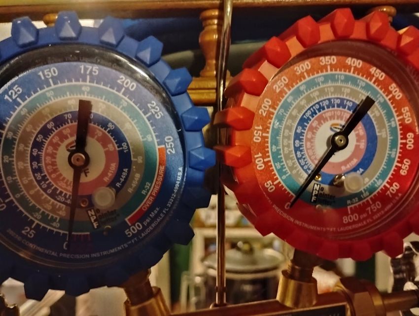 Blue and red HVAC pressure gauges with dials and needles on a brass manifold