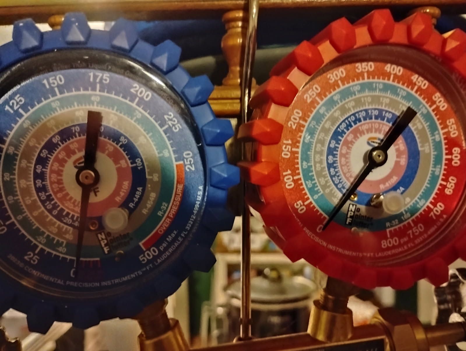 Blue and red HVAC gauge meters with dials and needles on a brass manifold