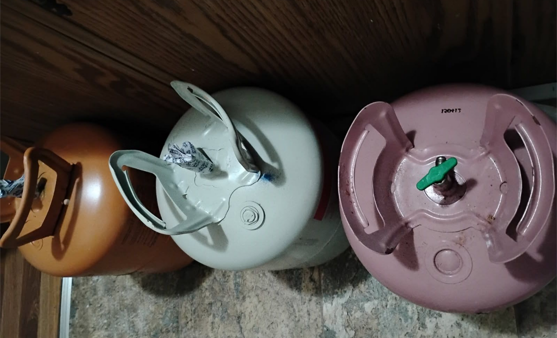 Three colorful gas cylinders lying on their sides against a wooden wall.