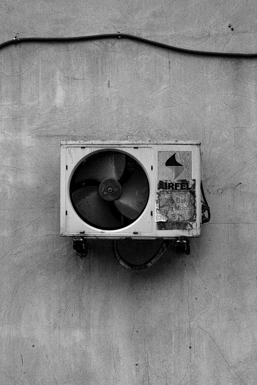 Wall-mounted air conditioner unit beneath a cable on a plain concrete wall.