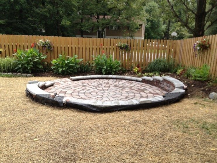 A brick patio is being built in a backyard next to a wooden fence.