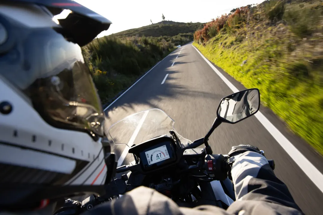 Motorcyclist riding on a sunlit winding road, helmet view with hills and mirror visible