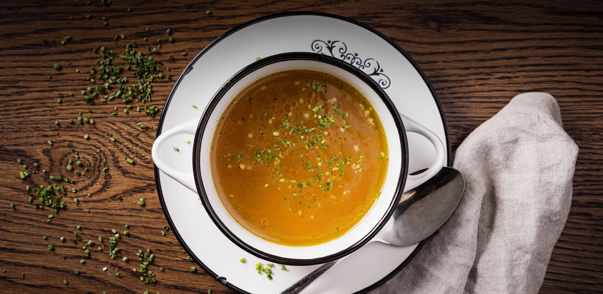 Eine Schüssel Suppe auf einer Untertasse mit einem Löffel auf einem Holztisch.