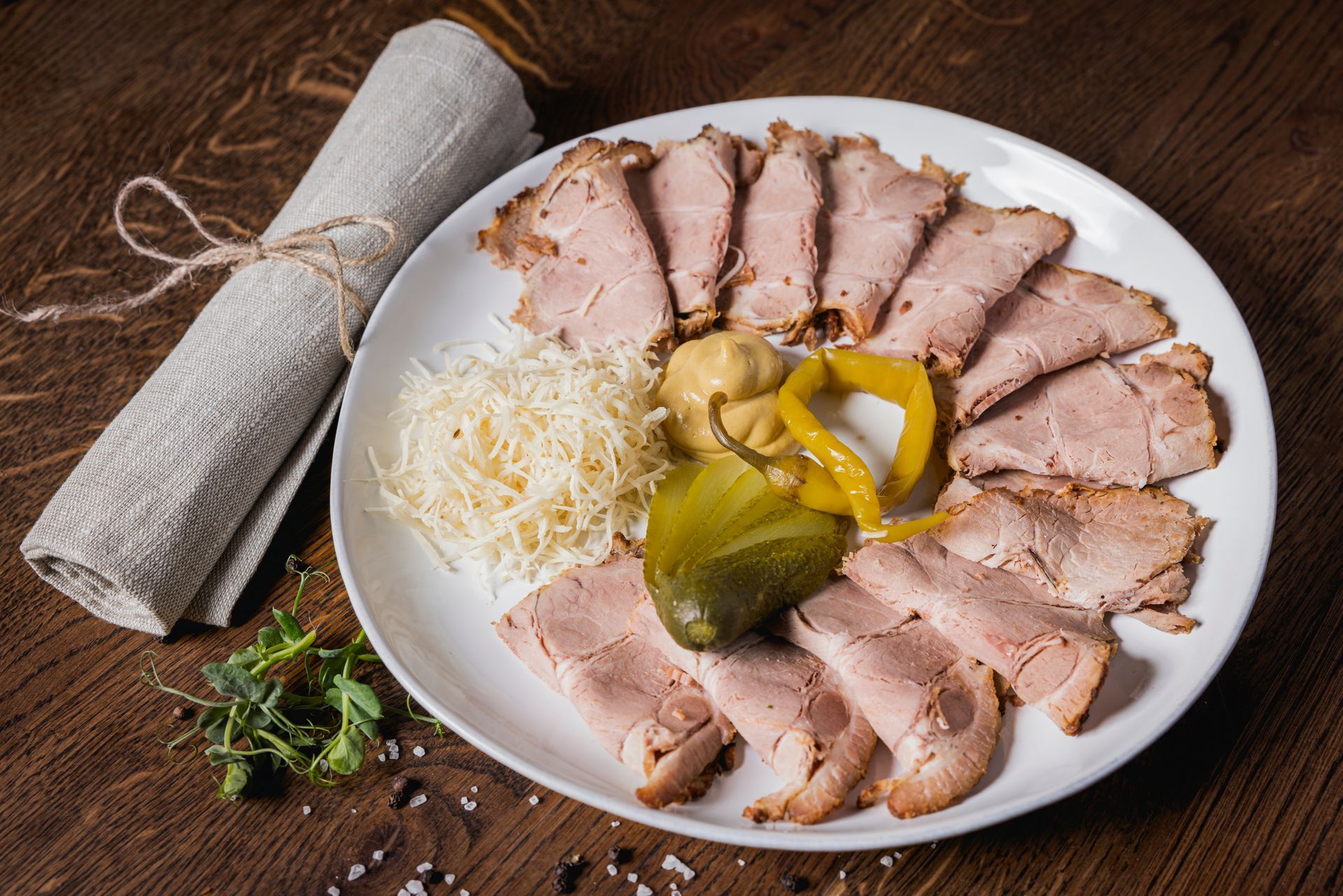 Ein weißer Teller mit geschnittenem Fleisch und eingelegten Gurken auf einem Holztisch.