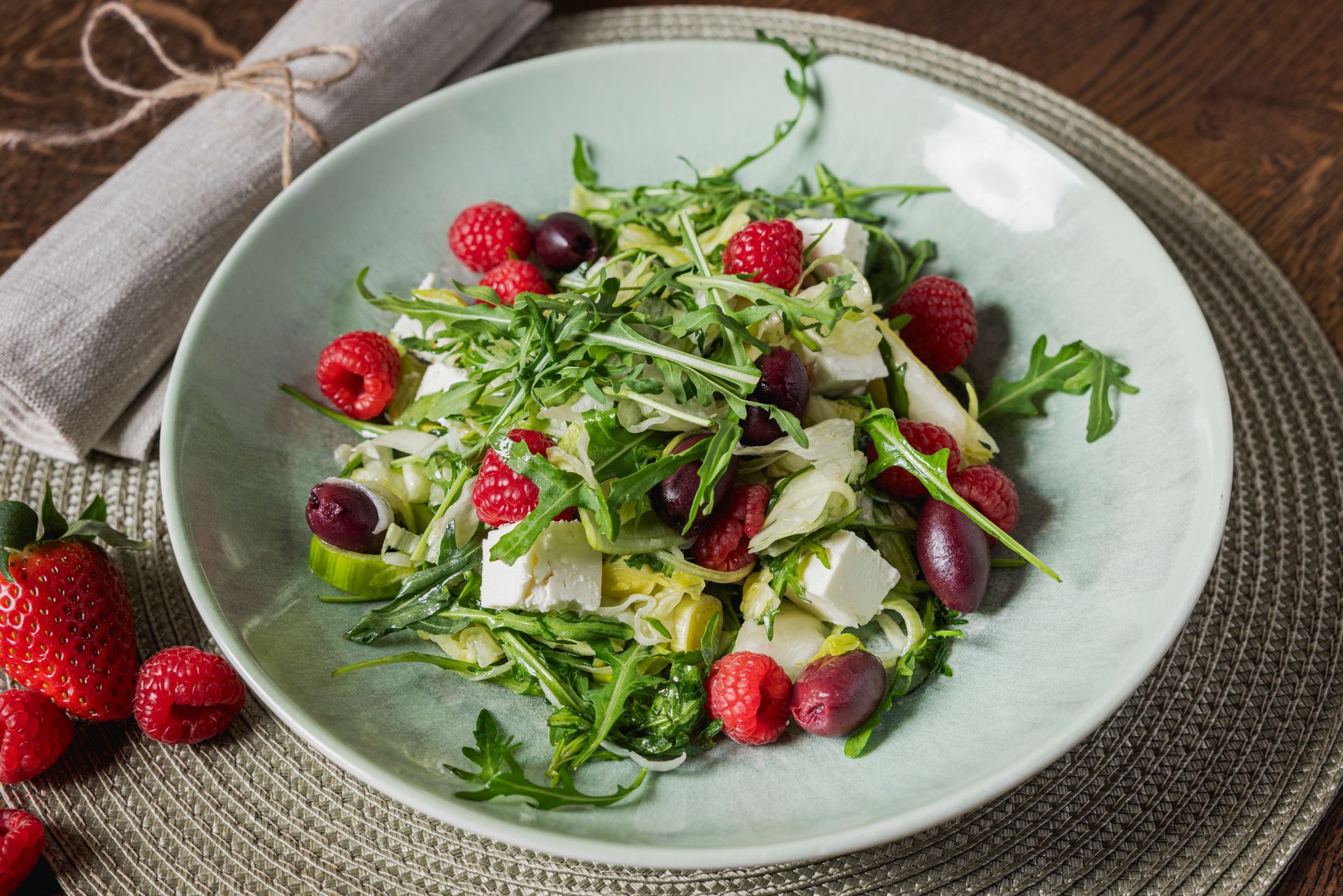 Ein Salat mit Himbeeren, Oliven, Fetakäse und Spargel auf einem Teller auf einem Tisch.
