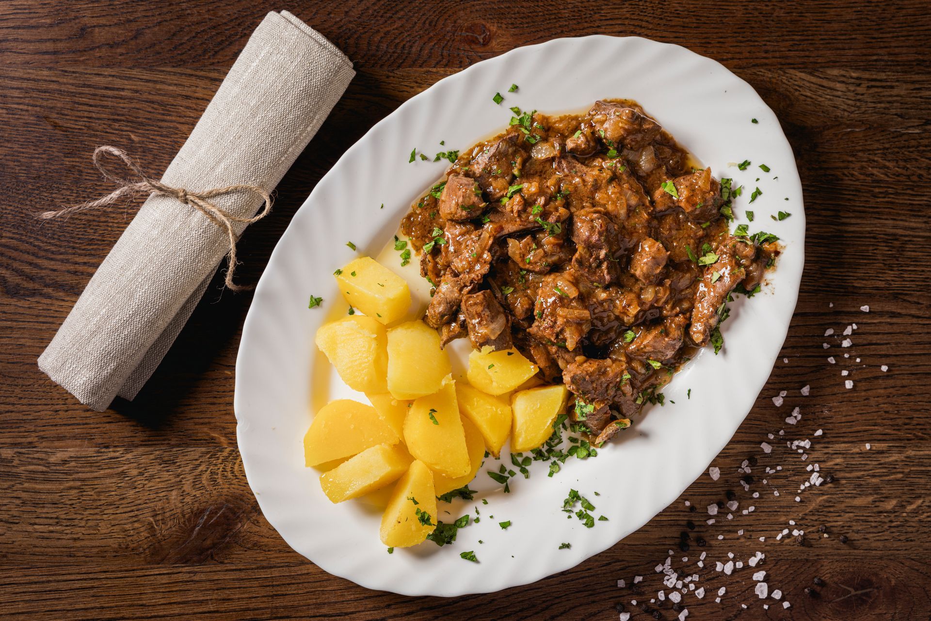 Ein weißer Teller mit Fleisch und Kartoffeln auf einem Holztisch.