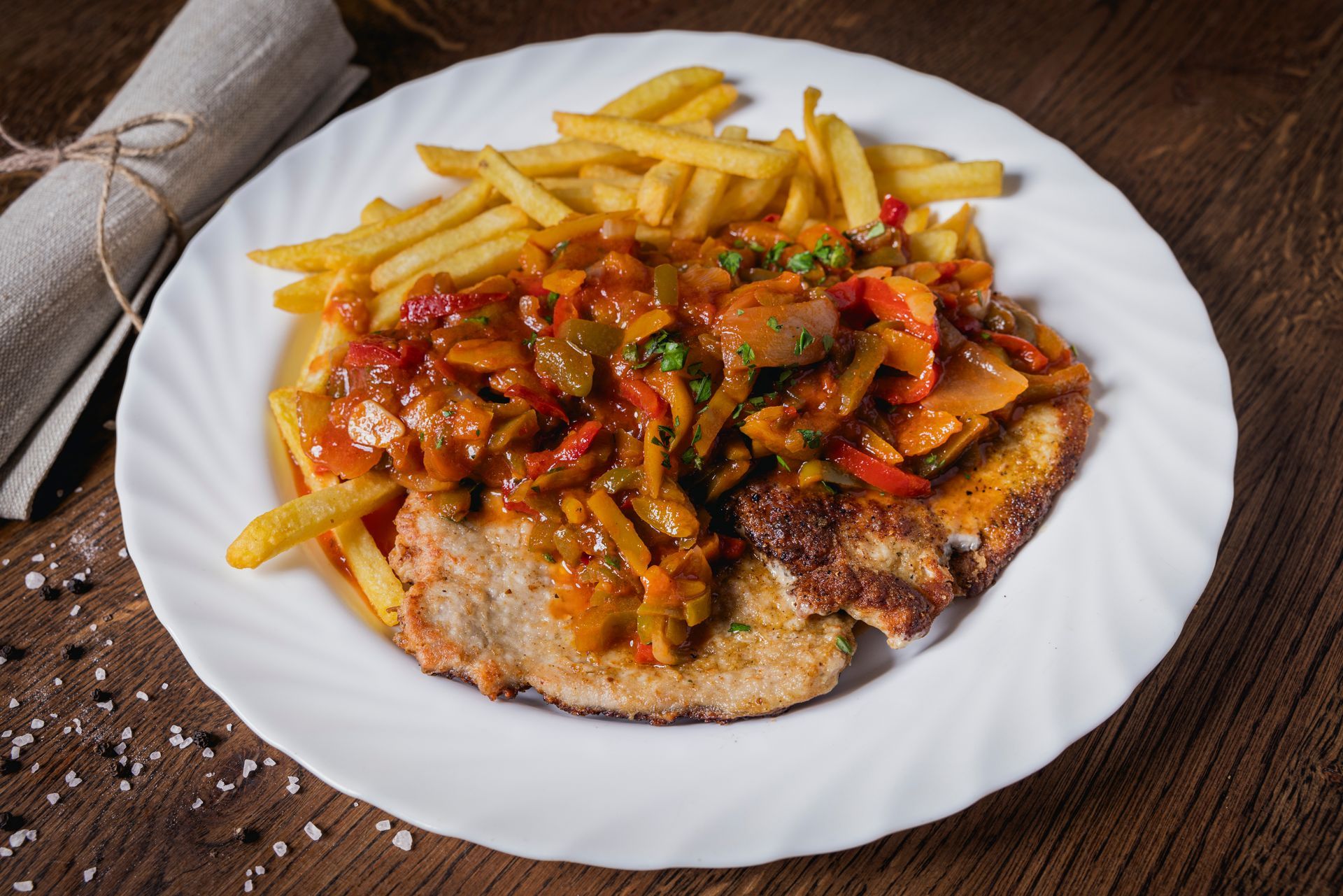 Ein weißer Teller mit Fleisch und Pommes Frites auf einem Holztisch.
