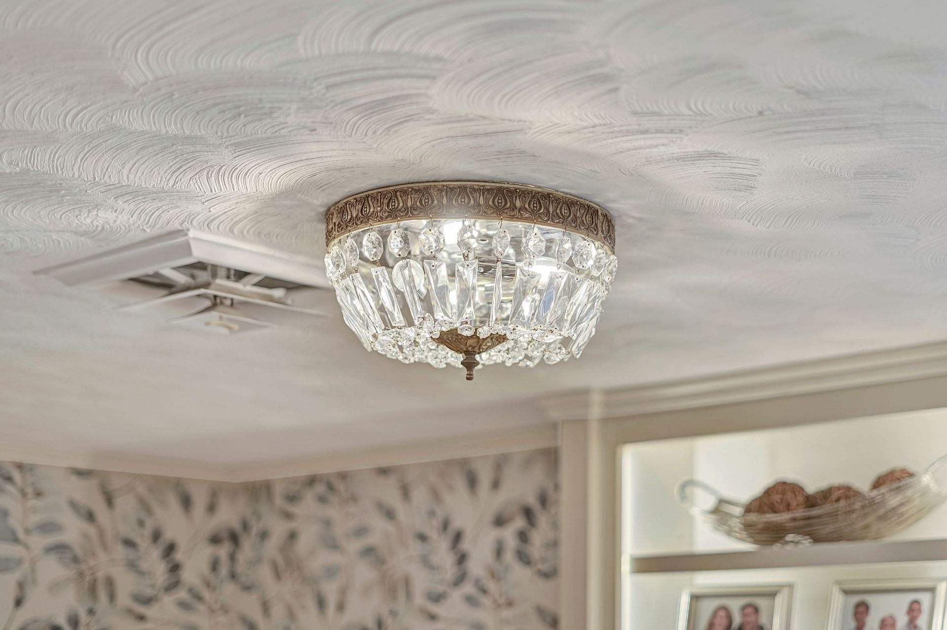 Crystal ceiling light fixture. Antique brass finish, surrounded by clear crystals, mounted to a textured white ceiling.
