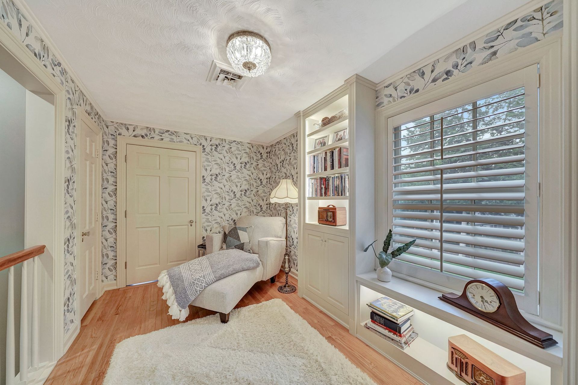 Cozy reading nook with a chaise lounge, built-in bookshelf, and window with blinds.