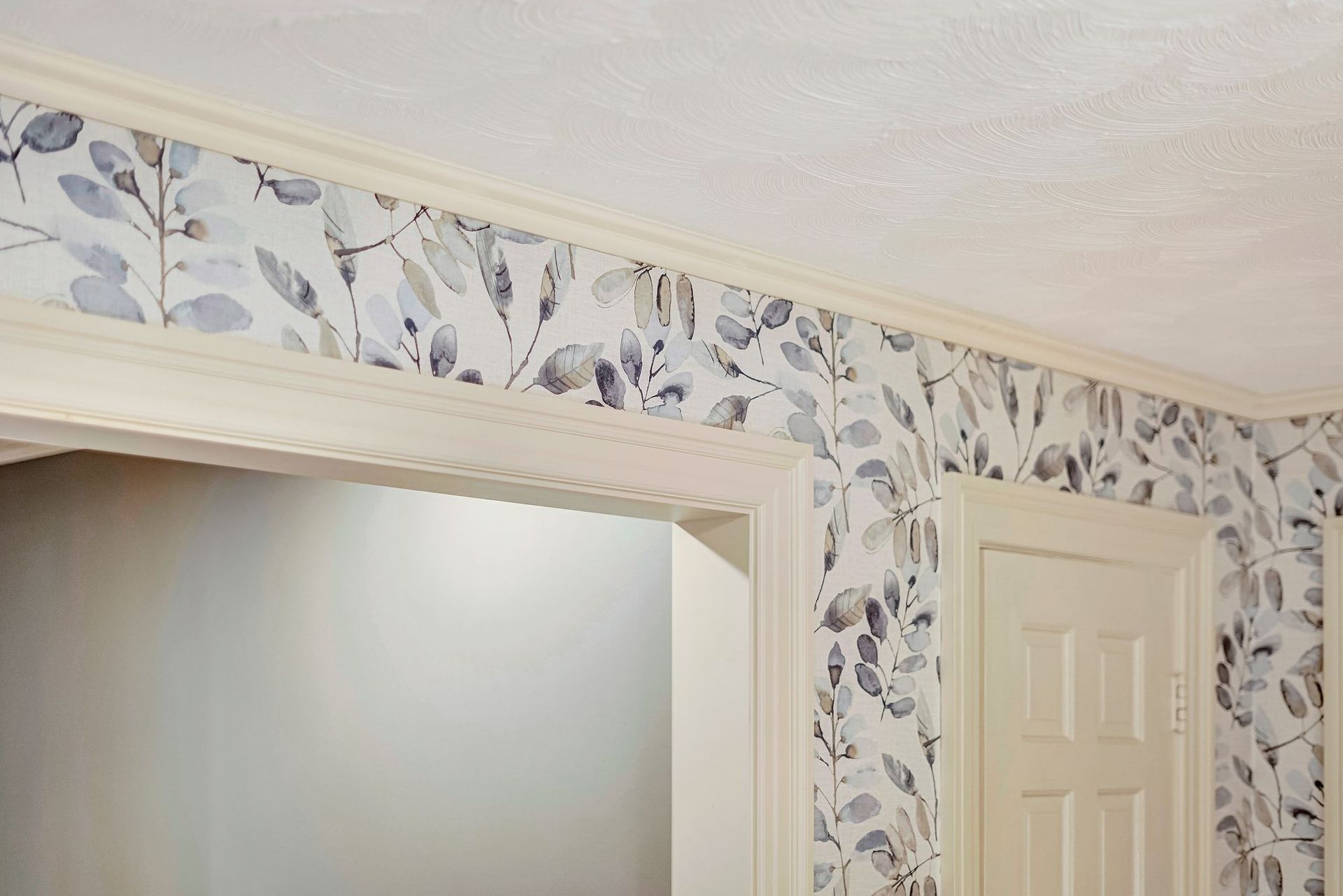 Room corner with botanical wallpaper, white trim, and a doorway.
