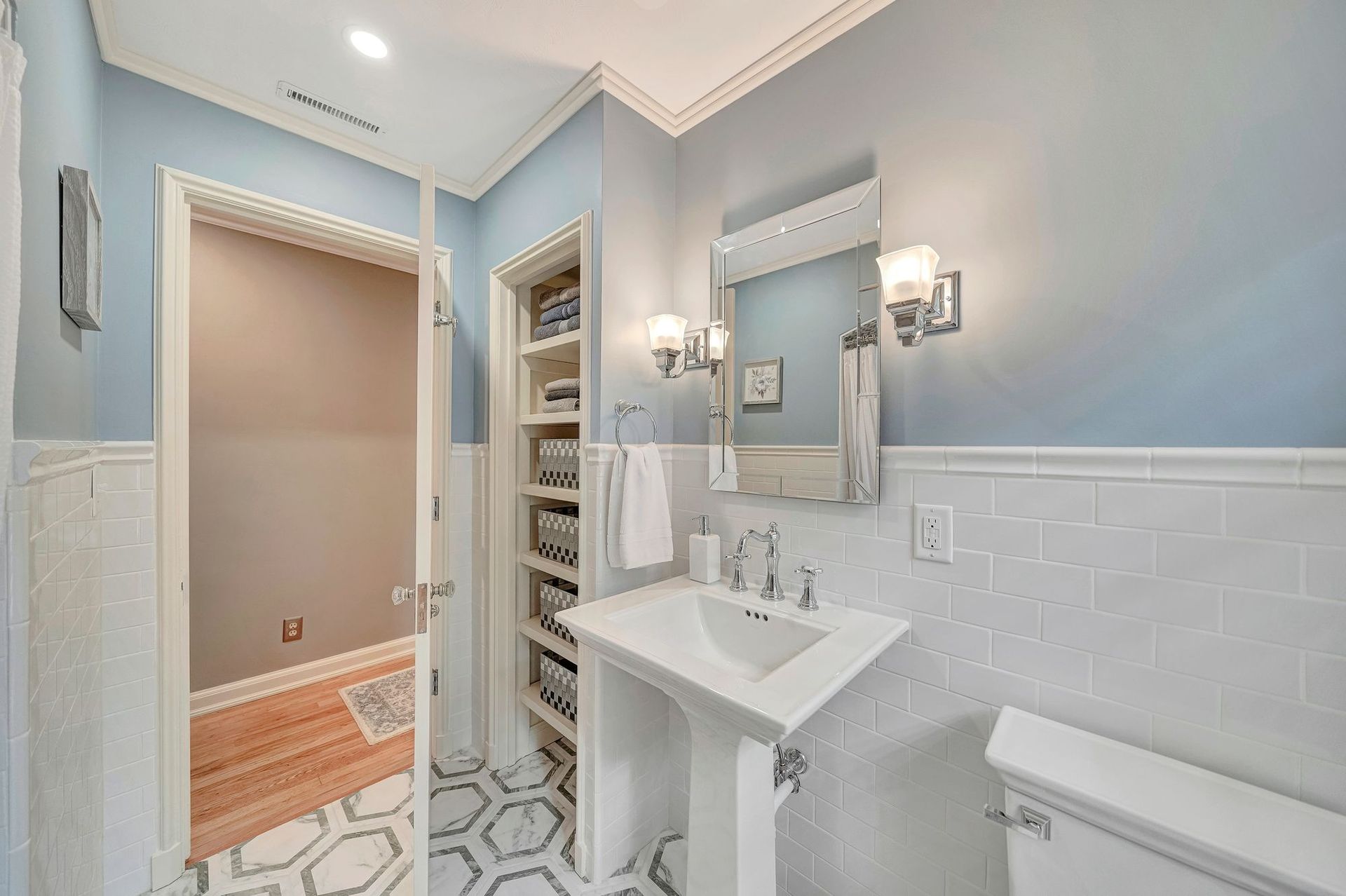 Bathroom with light blue walls, white pedestal sink, and built-in shelving.