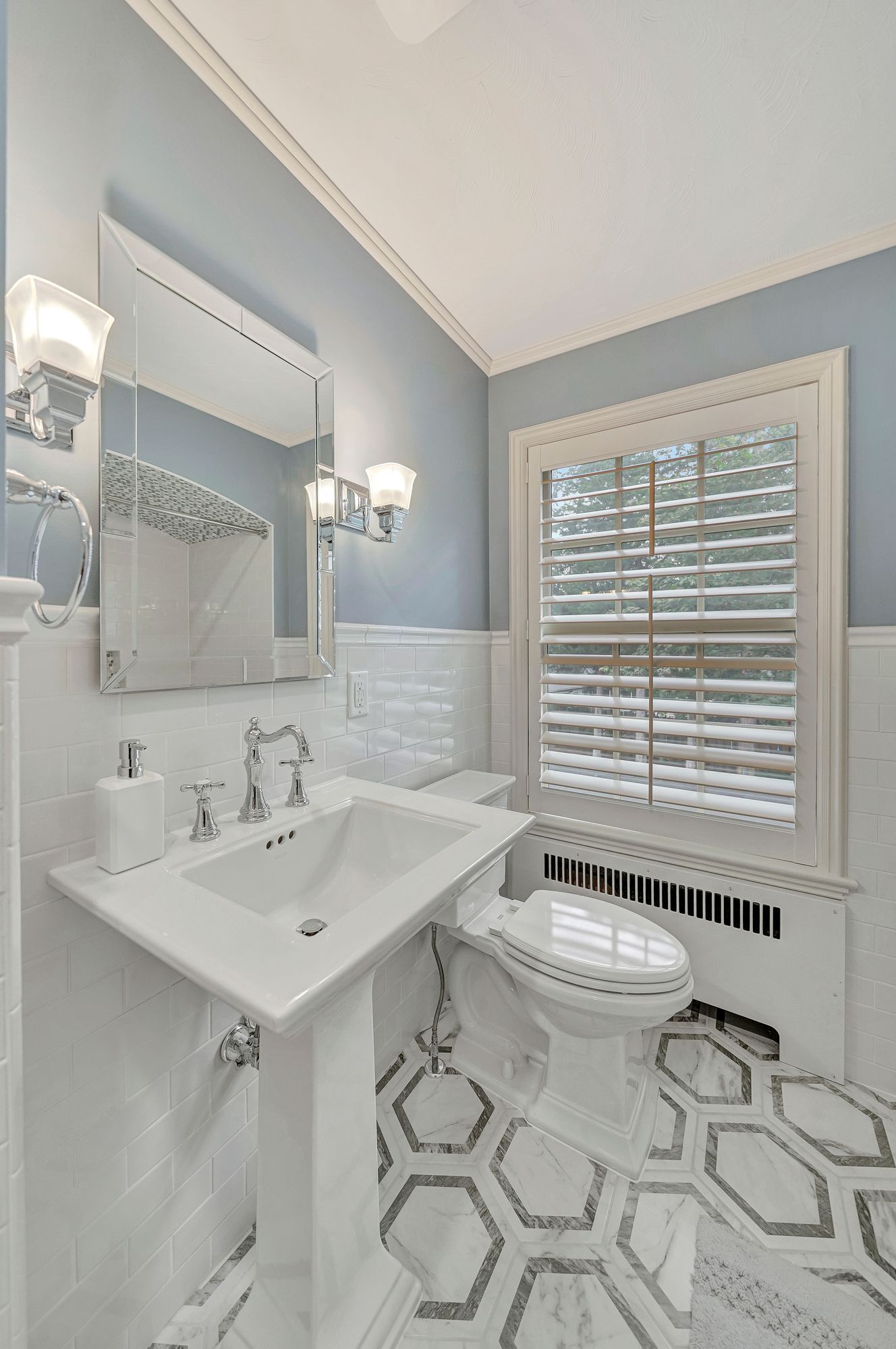 Bathroom with pedestal sink, toilet, window with blinds, and hexagon tile floor.