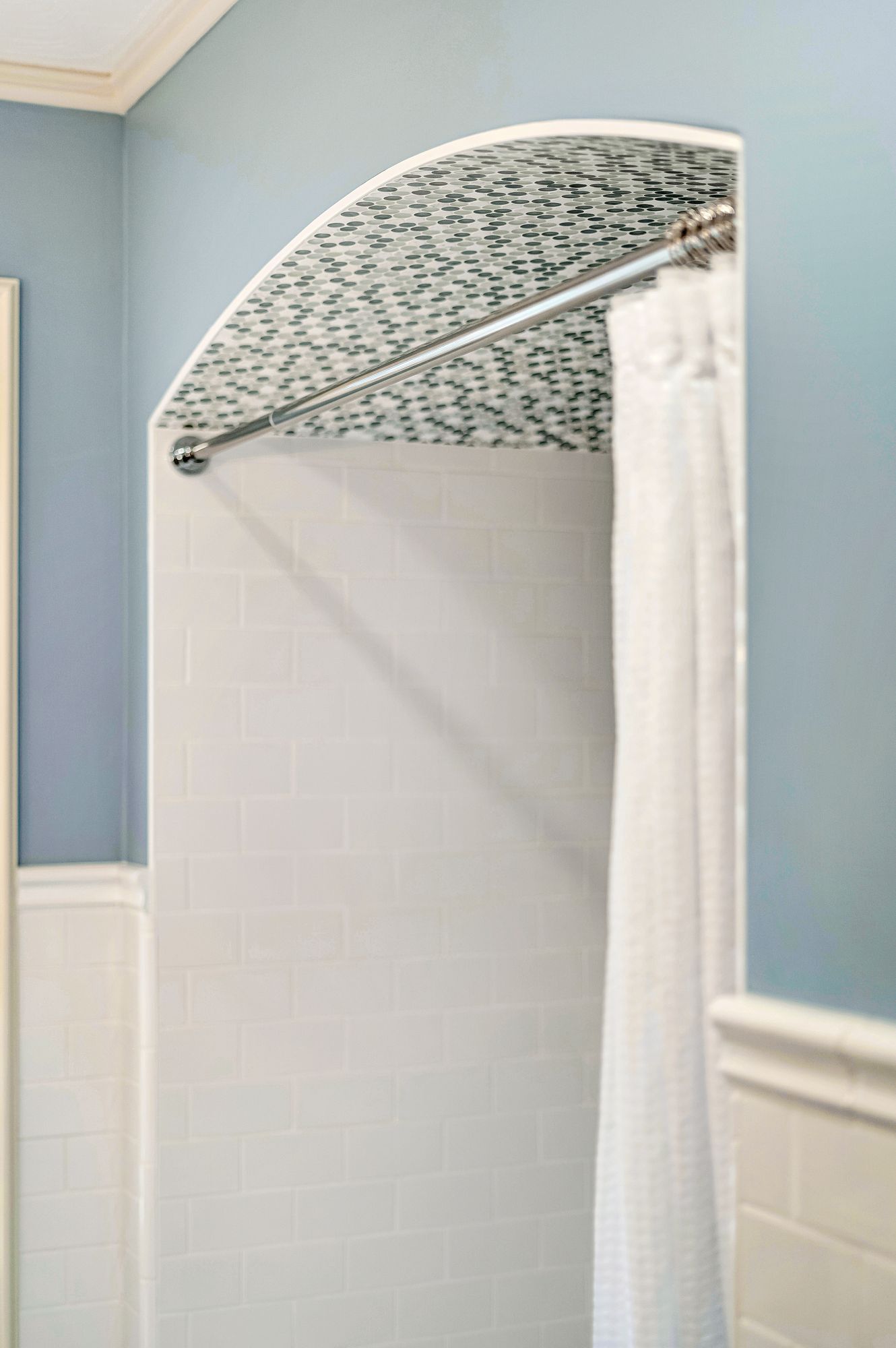 Shower with curved mosaic tile ceiling, white walls, and a curtain rod with a white shower curtain.
