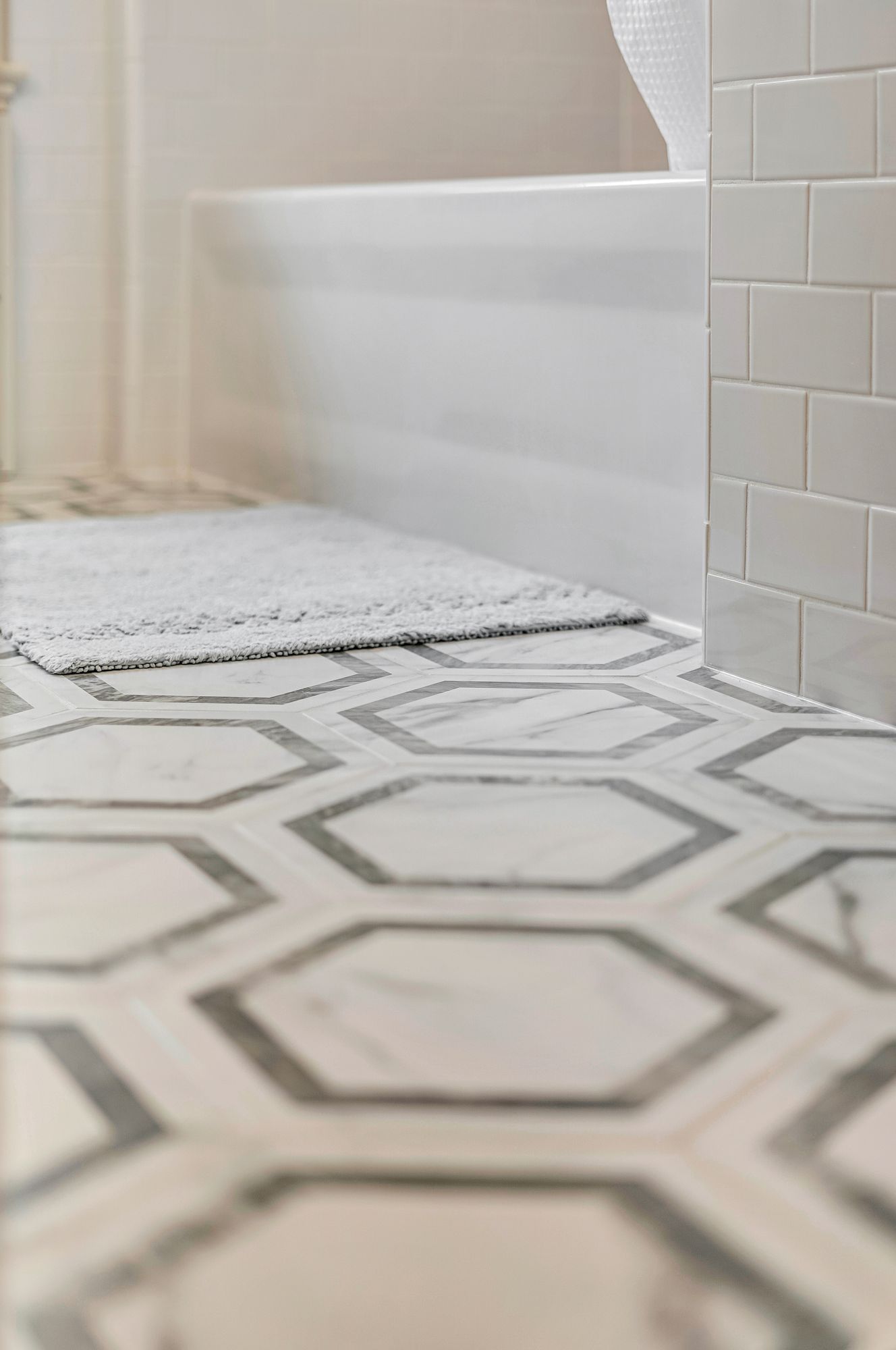 Bathroom floor with hexagonal marble tiles, rug, and white bathtub.