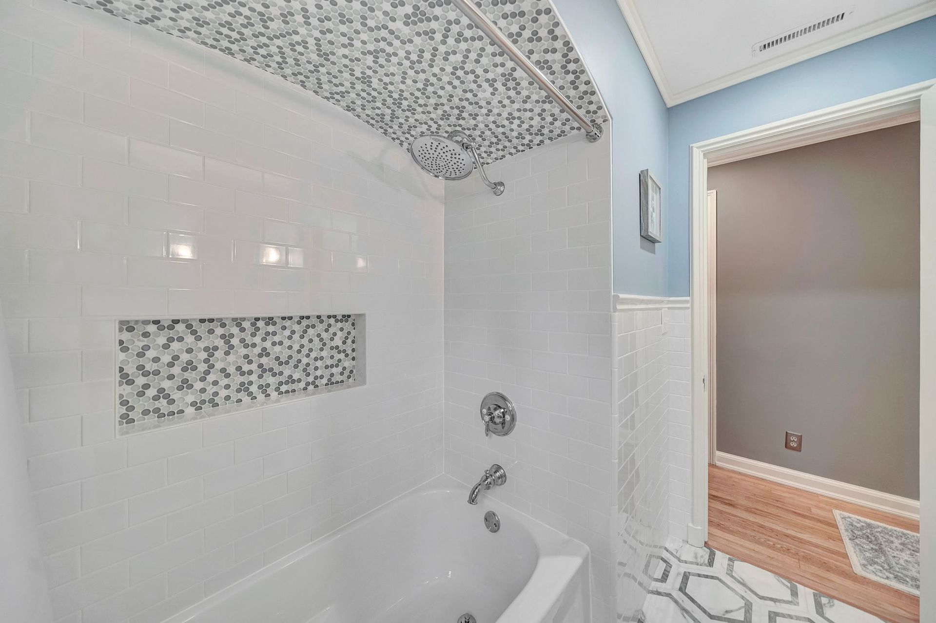 White tiled bathroom with mosaic tile accents, a bathtub, and a doorway.