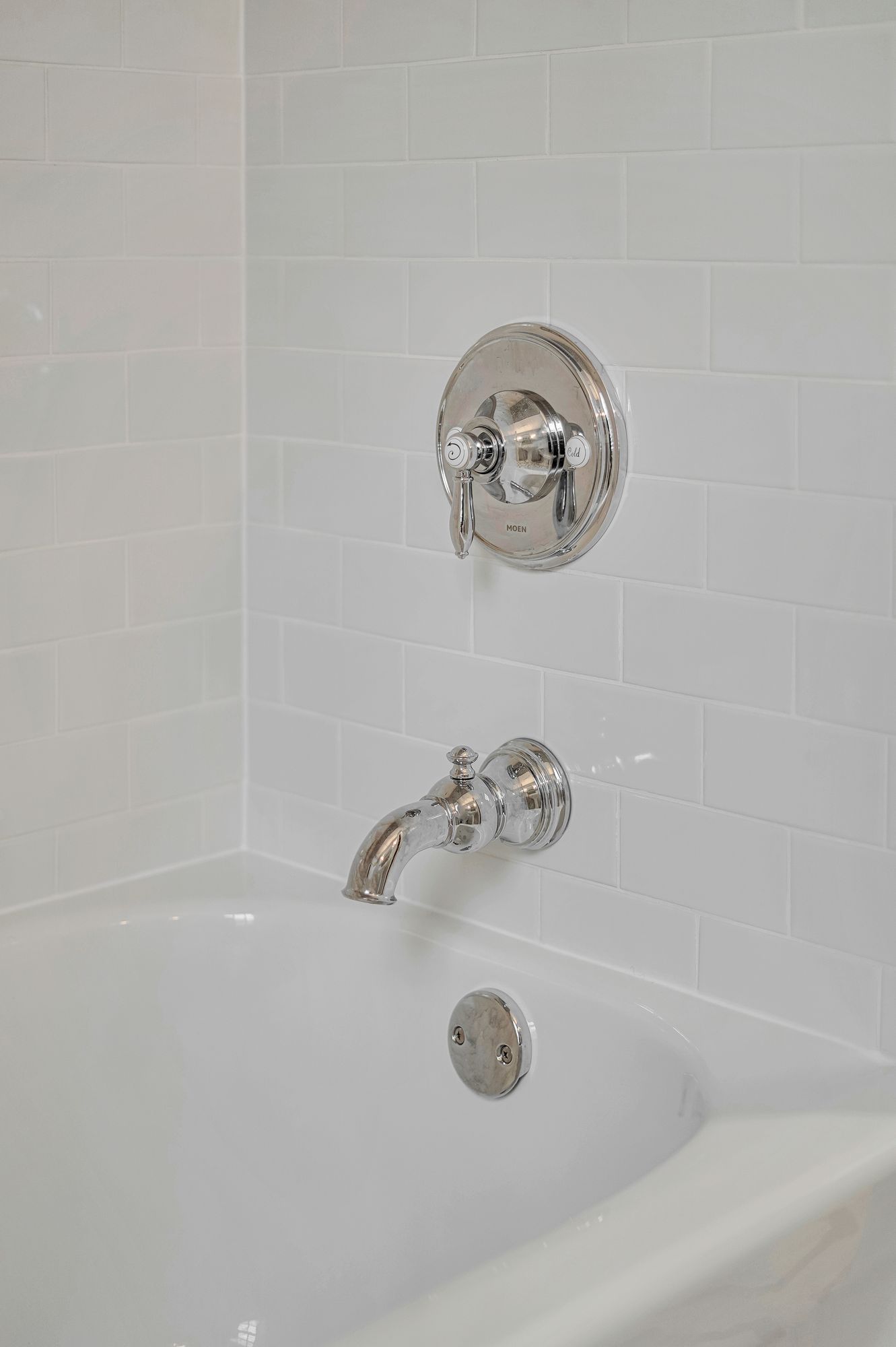 White tiled bathroom with chrome faucet, showerhead, and bathtub.