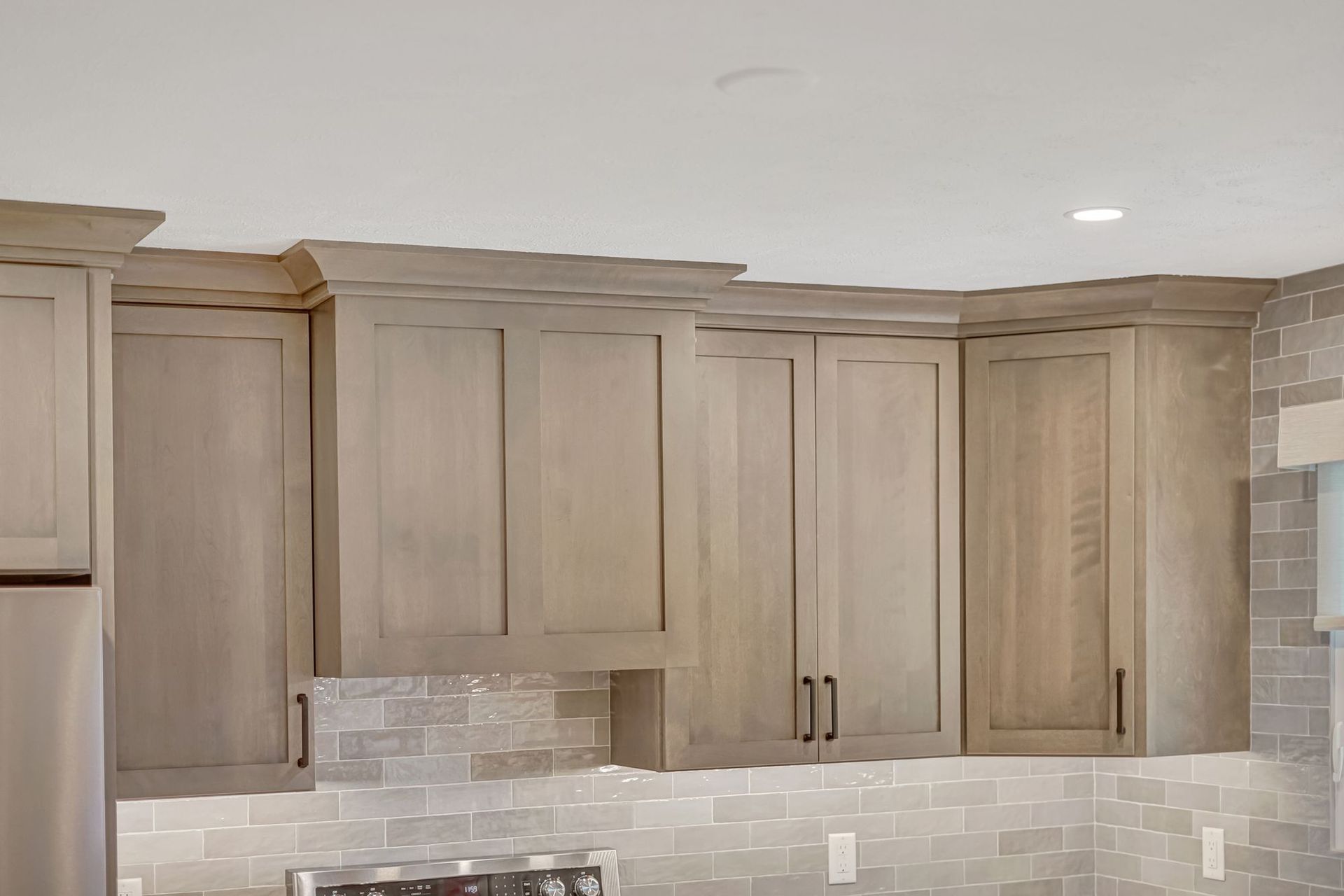 Light grey kitchen cabinets with crown molding and dark hardware against a light grey backsplash.