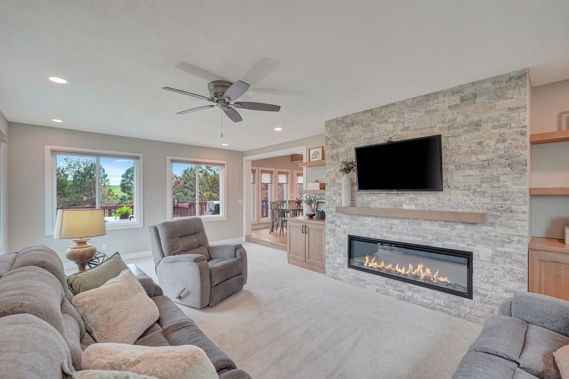 Living room with stone fireplace, TV, recliner, couch, windows. Neutral colors.