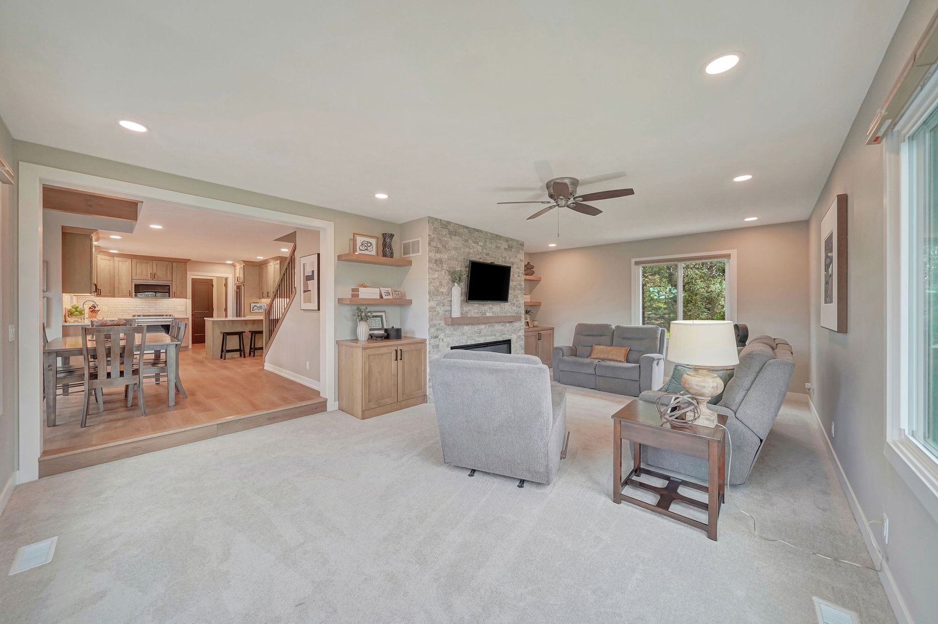 Living room with open view to kitchen, neutral color scheme, fireplace, and seating.