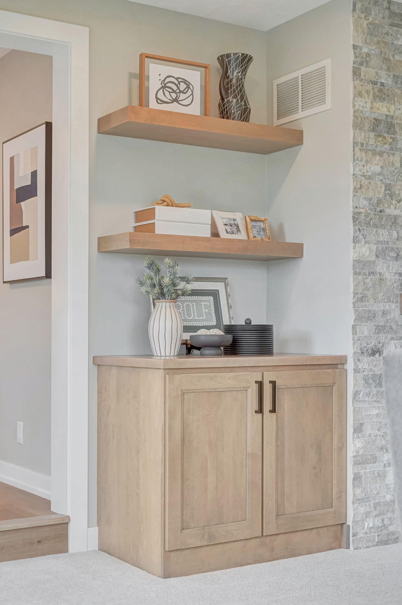Built-in shelves and cabinet in a neutral-toned corner. Shelves hold decor; cabinet has two doors with black handles.