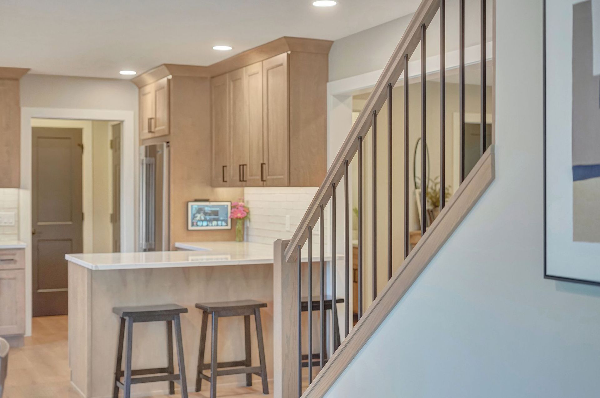 Kitchen with light wood cabinets, white countertops, and a staircase with black spindles.