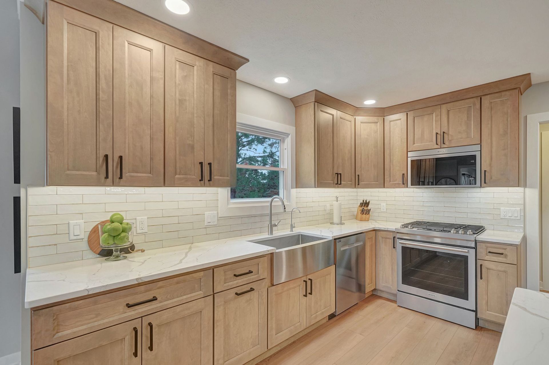 Kitchen with light wood cabinets, white countertops, stainless steel appliances, and a window.