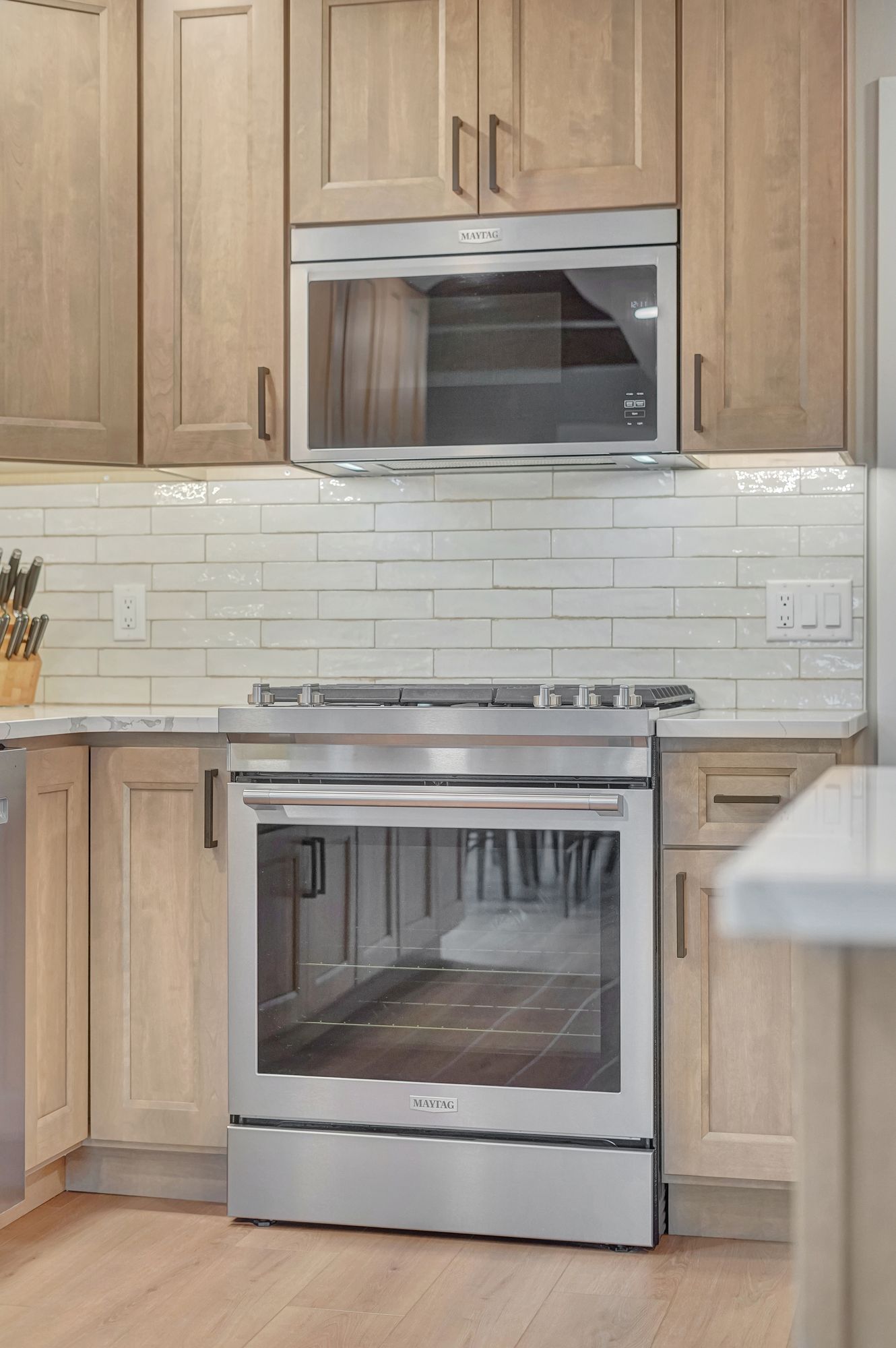 Stainless steel oven and microwave in a kitchen with light wood cabinets and white backsplash.