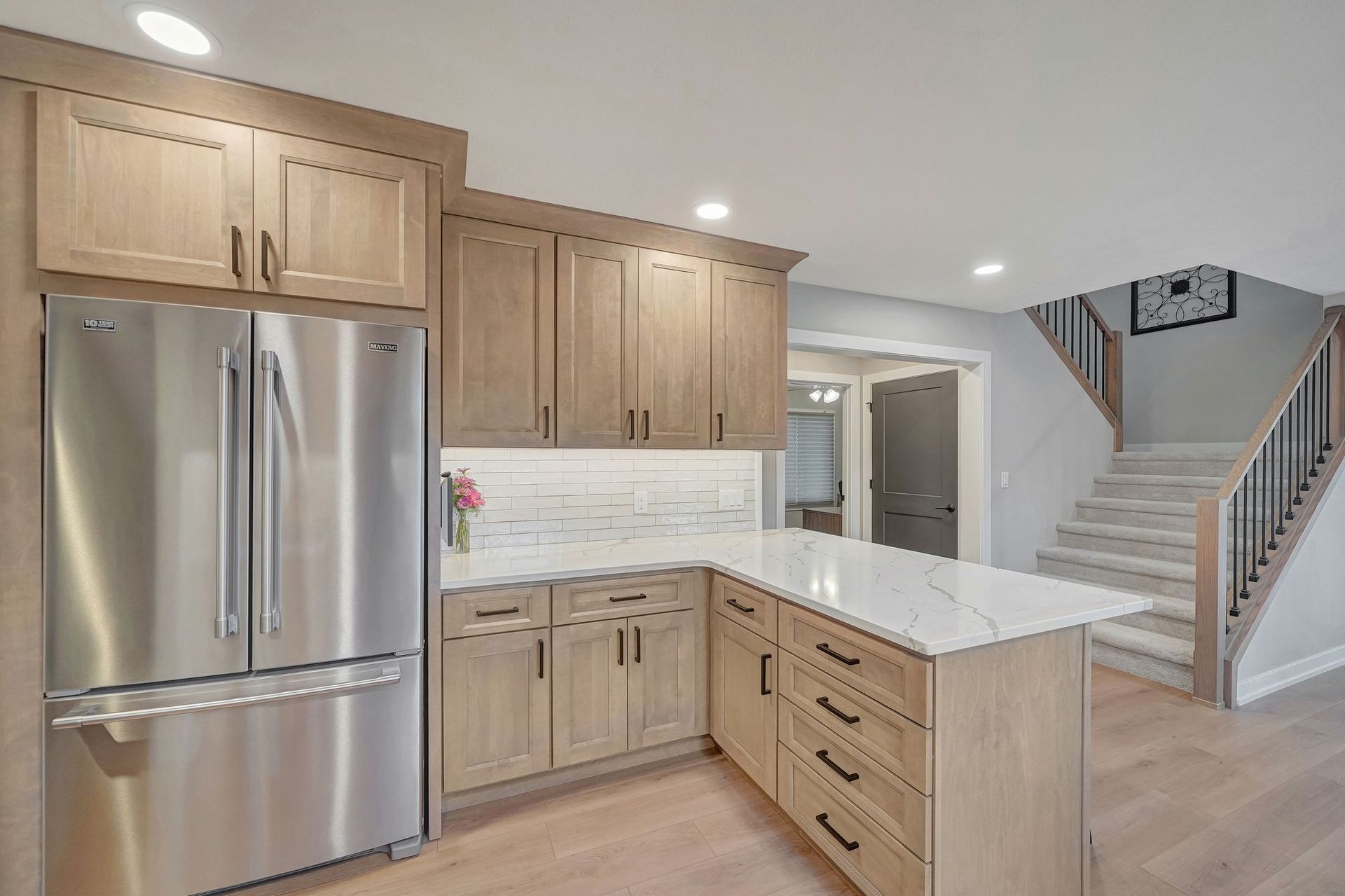 Modern kitchen with light wood cabinets, stainless steel refrigerator, and a white countertop island.
