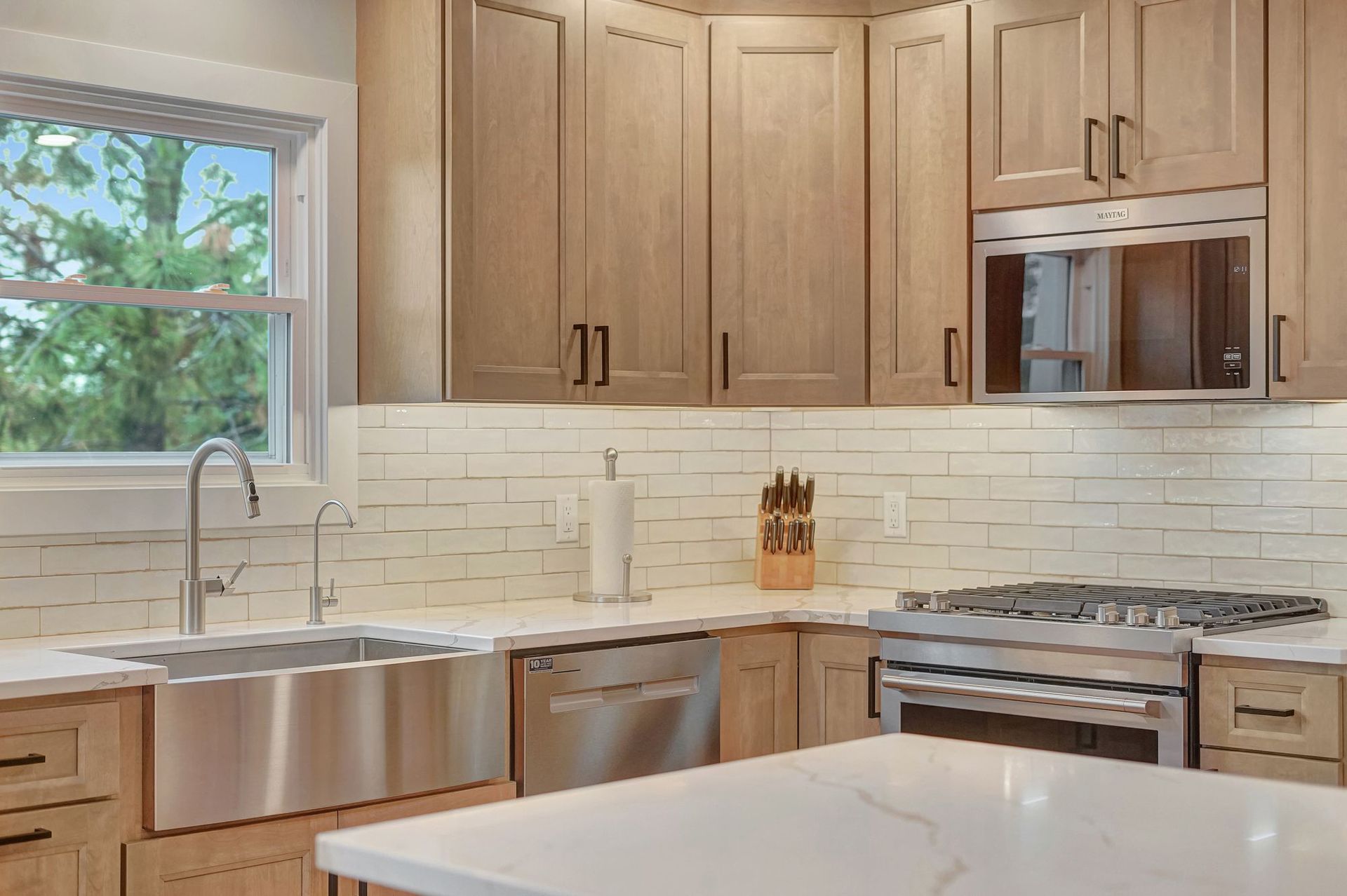 Modern kitchen with light wood cabinets, stainless steel appliances, and white countertops.