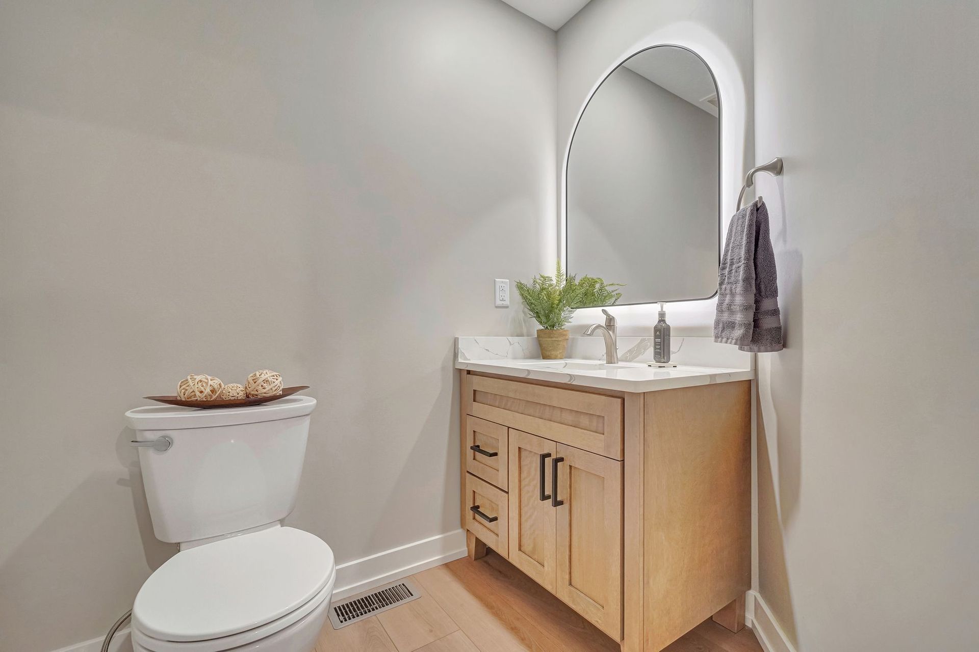 Bathroom with light wood vanity, arched mirror, and white toilet.
