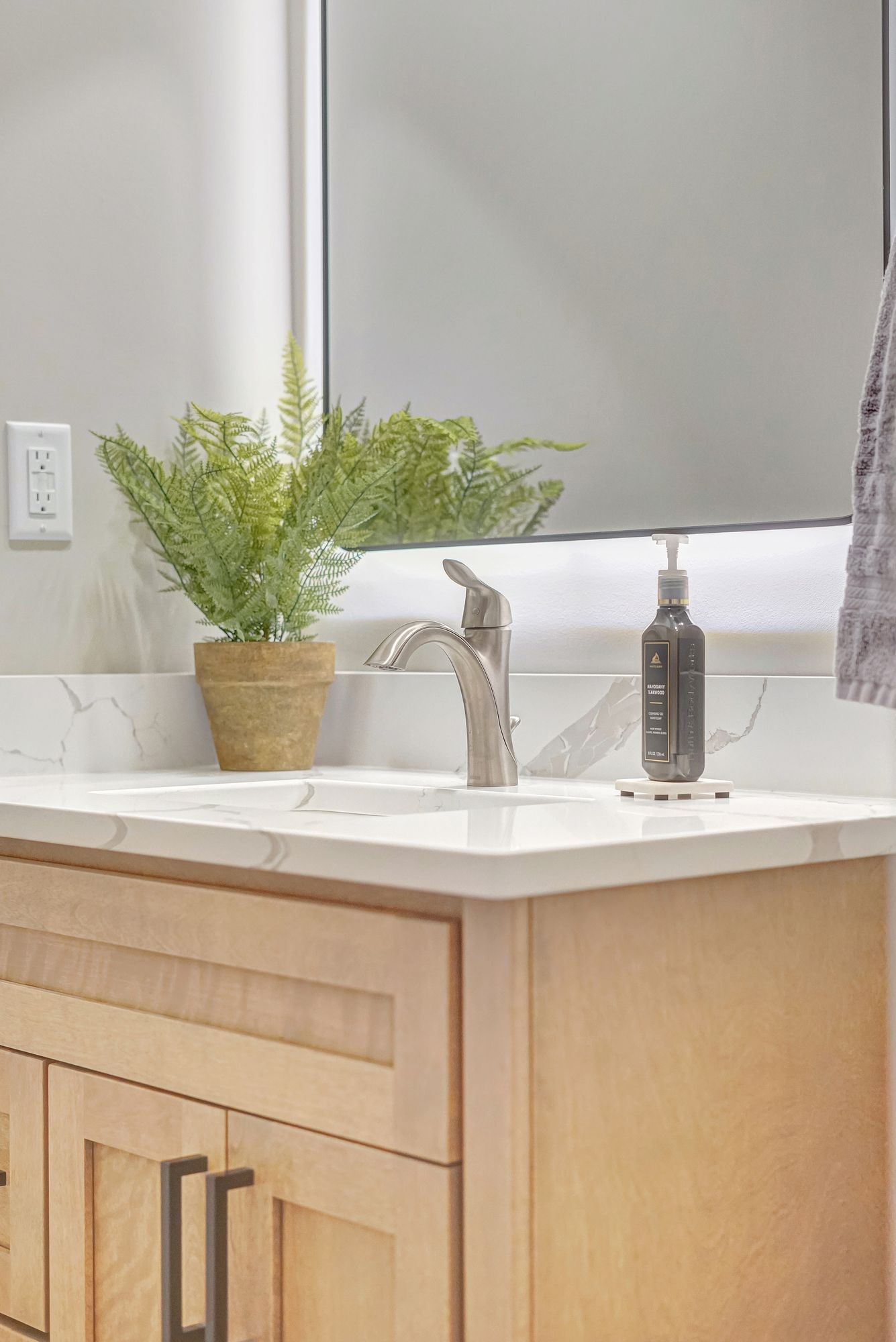 Bathroom vanity with light wood cabinets, white countertop, and faux plant.