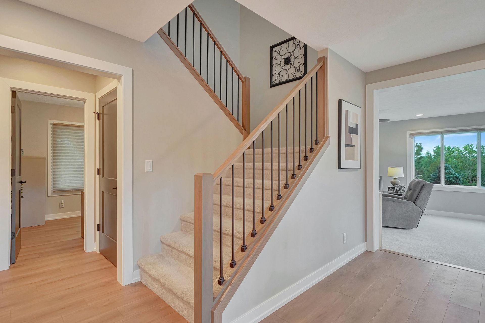 A light-filled entryway with stairs, tan wood floors, light gray walls, and a view into other rooms.