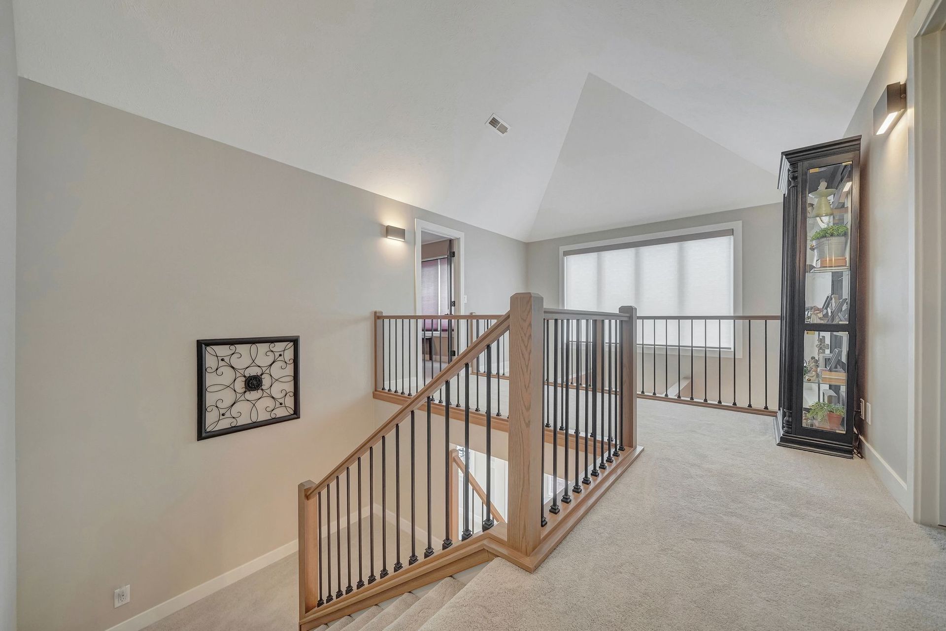 Loft area with staircase, beige carpet, gray walls, and a tall display cabinet.