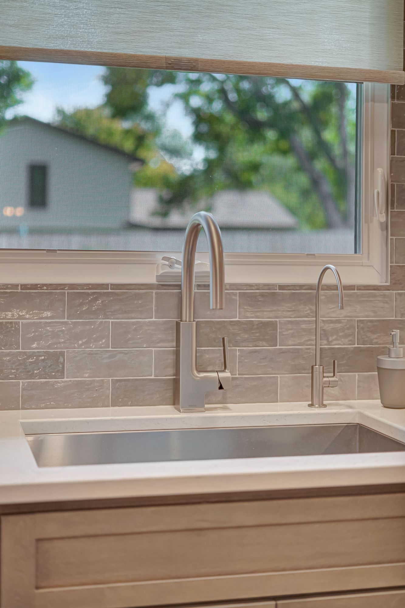 Kitchen sink with stainless steel faucet, and tile backsplash, window with trees outside.