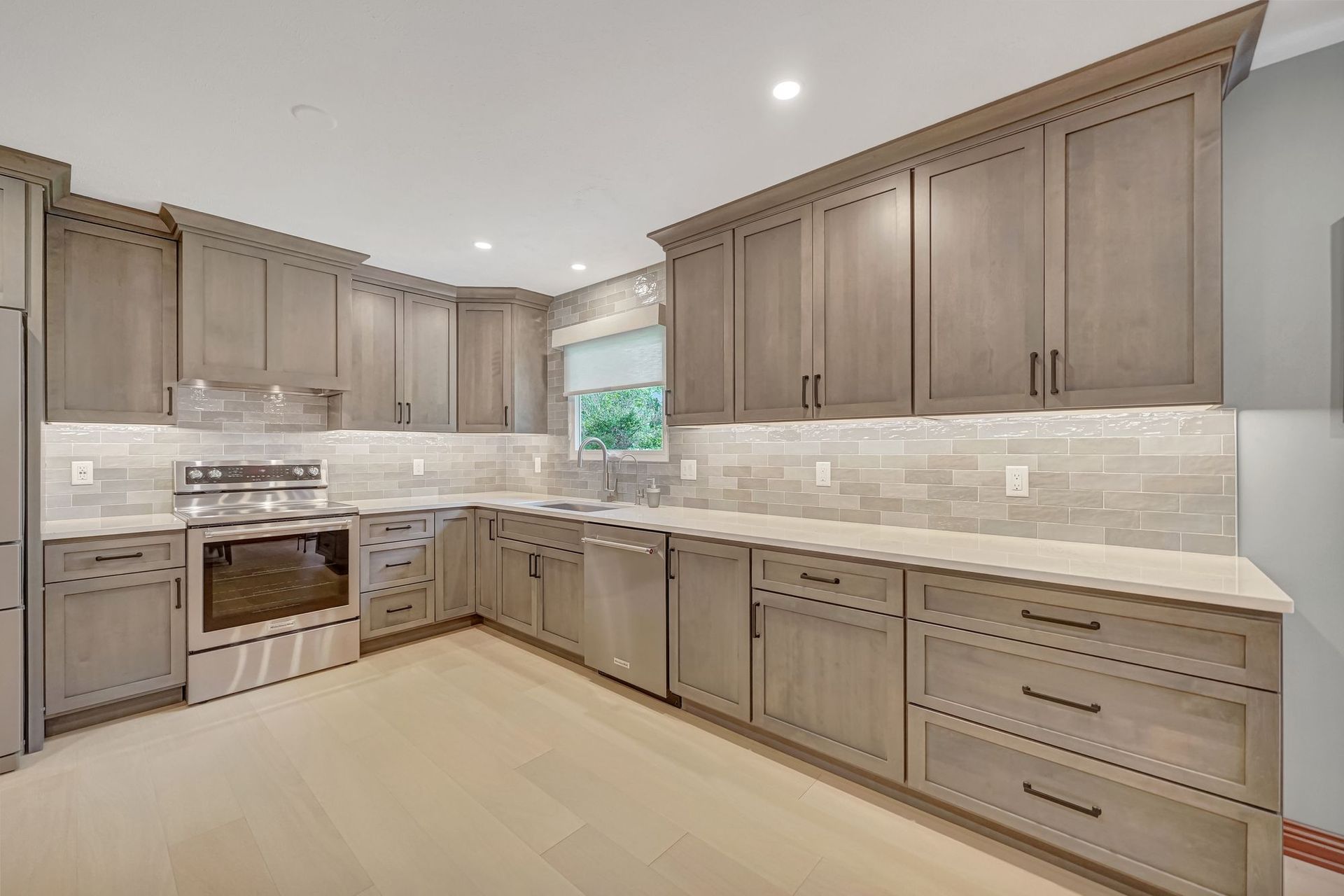 Kitchen with light gray cabinets, countertops, and tiled backsplash. Light wood flooring.
