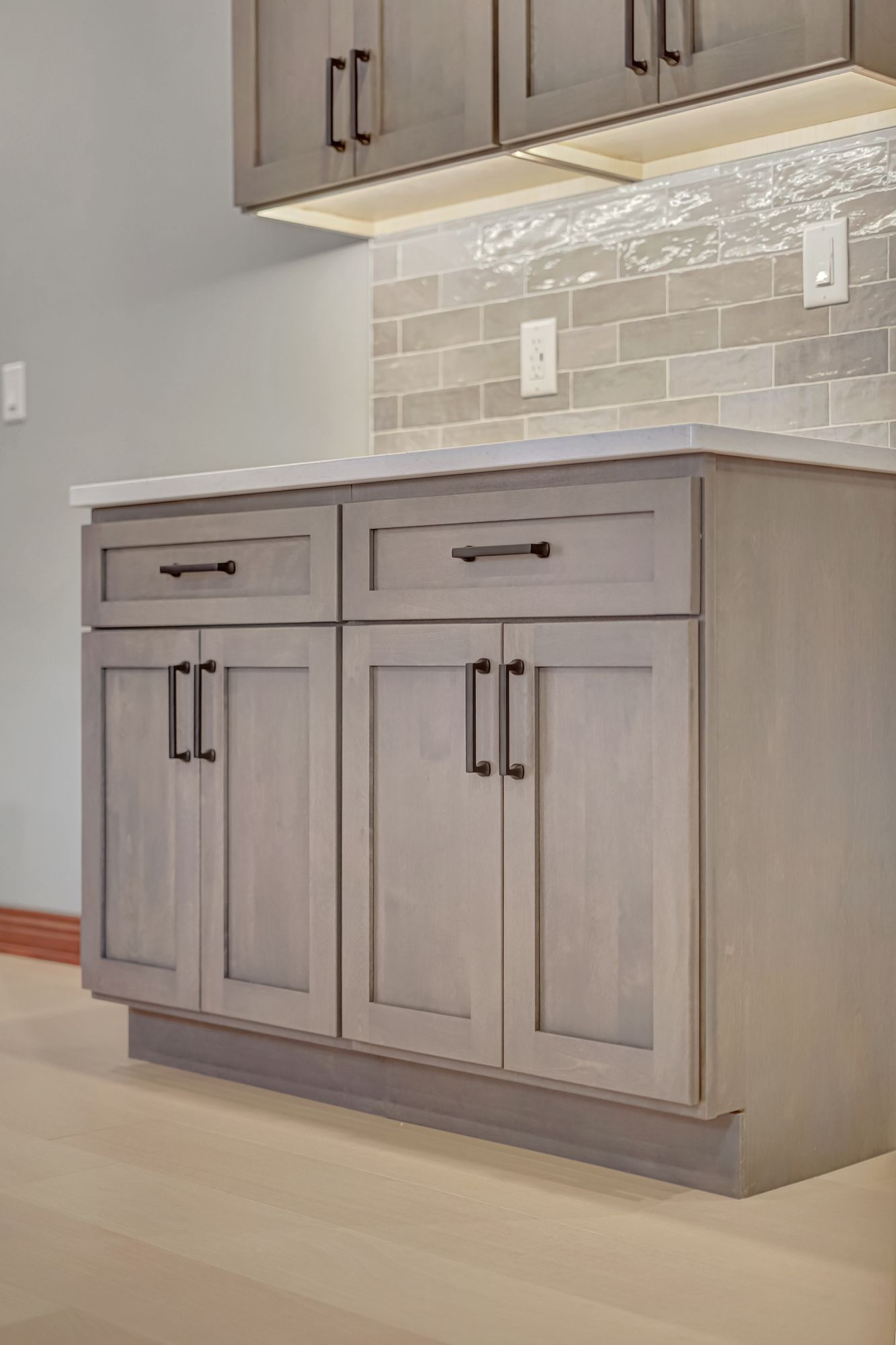 Gray kitchen cabinets with black hardware and white countertop; gray tile backsplash.