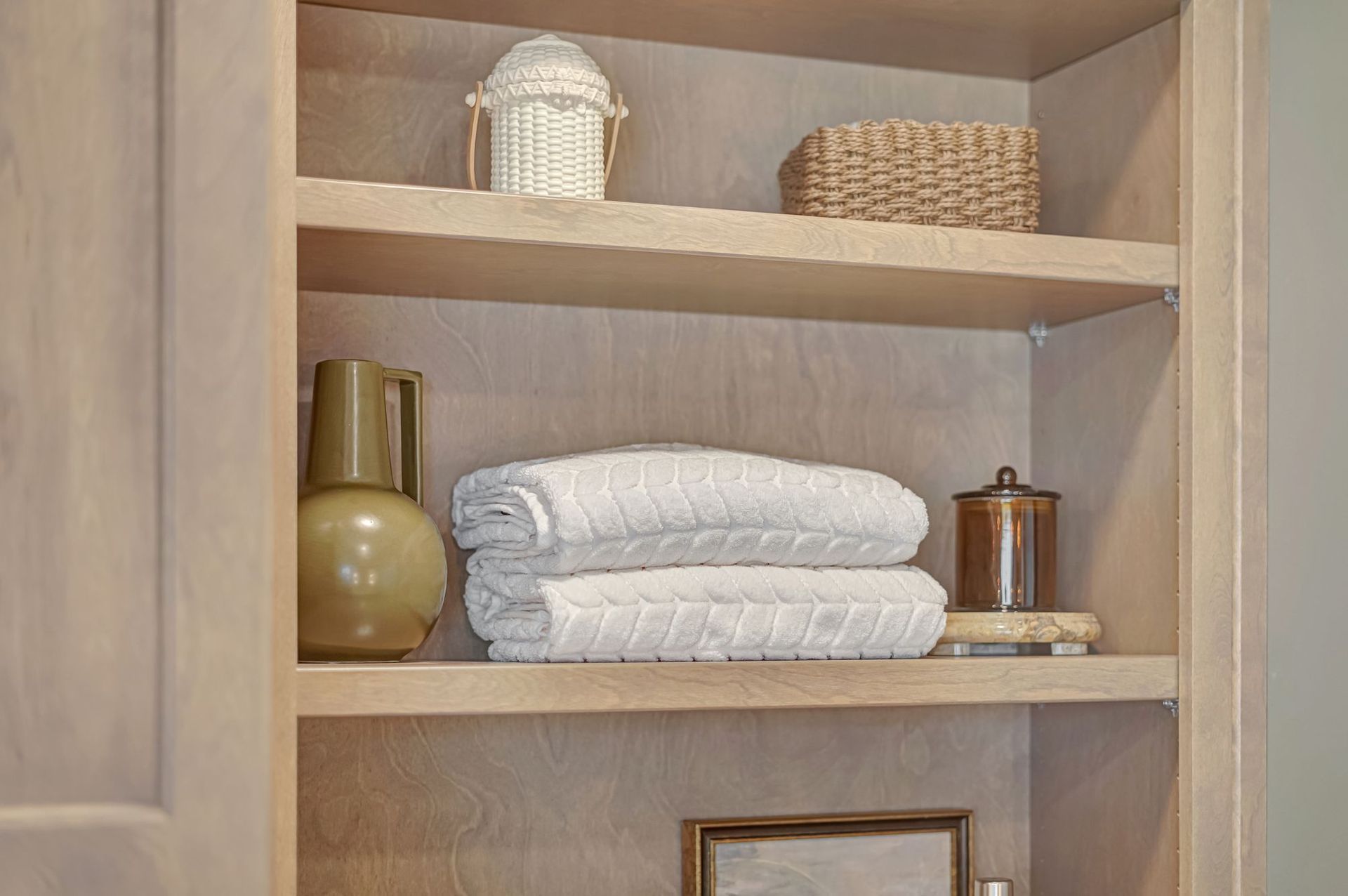 Wooden cabinet with shelves. Decorative items include towels, jars, and woven decor.