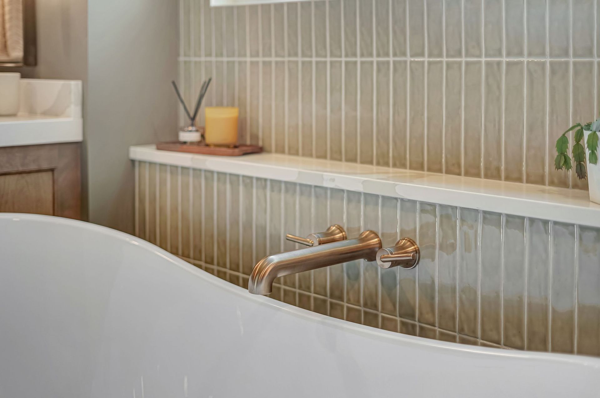 White bathtub with gold faucet against vertical gray tile wall.