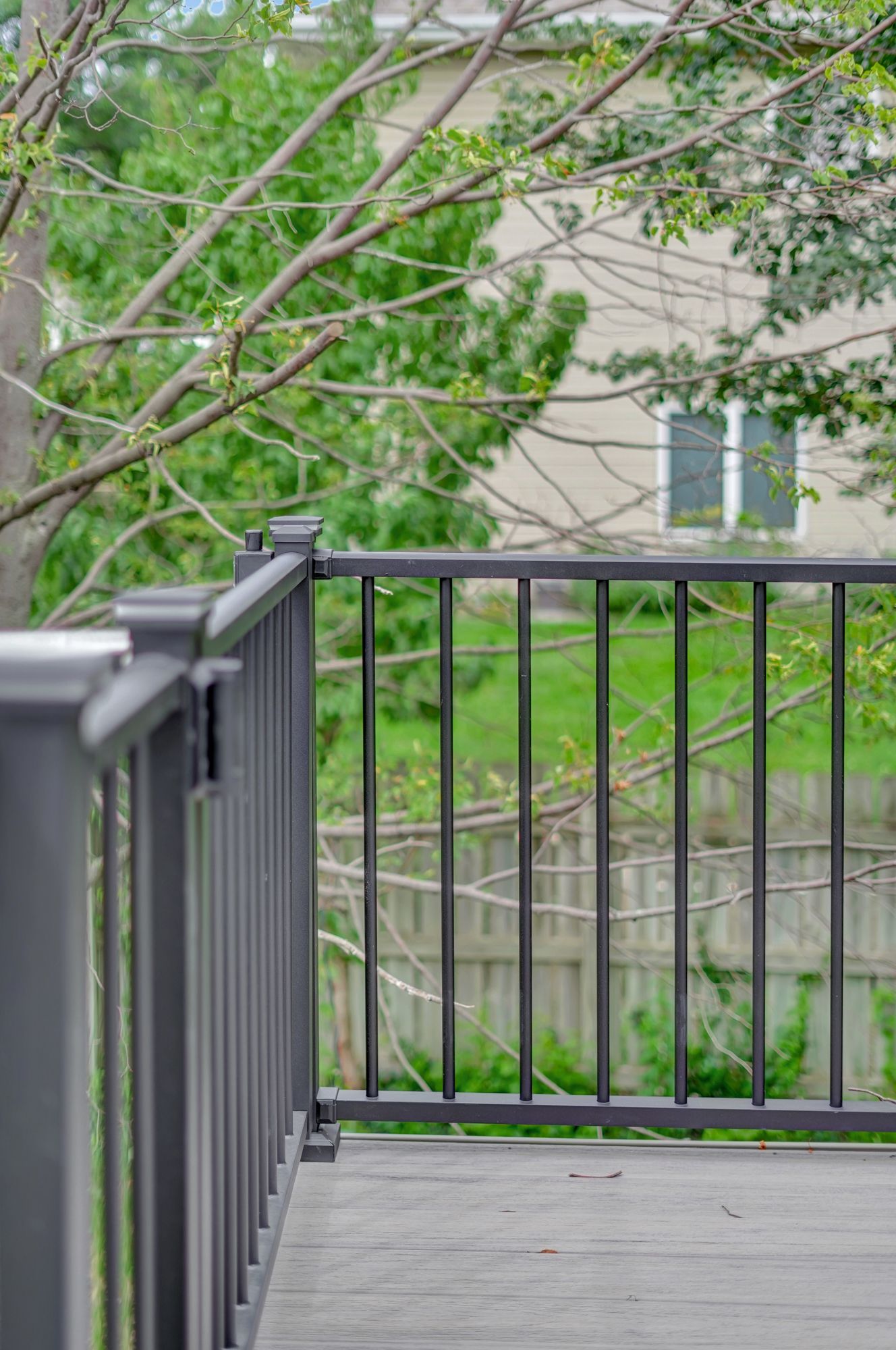 A deck with a metal railing and a view of a house and trees.