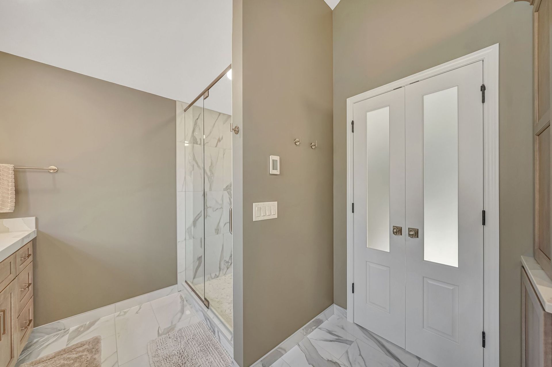 Bathroom interior with marble tile floor, shower, and closed white door. Beige walls.