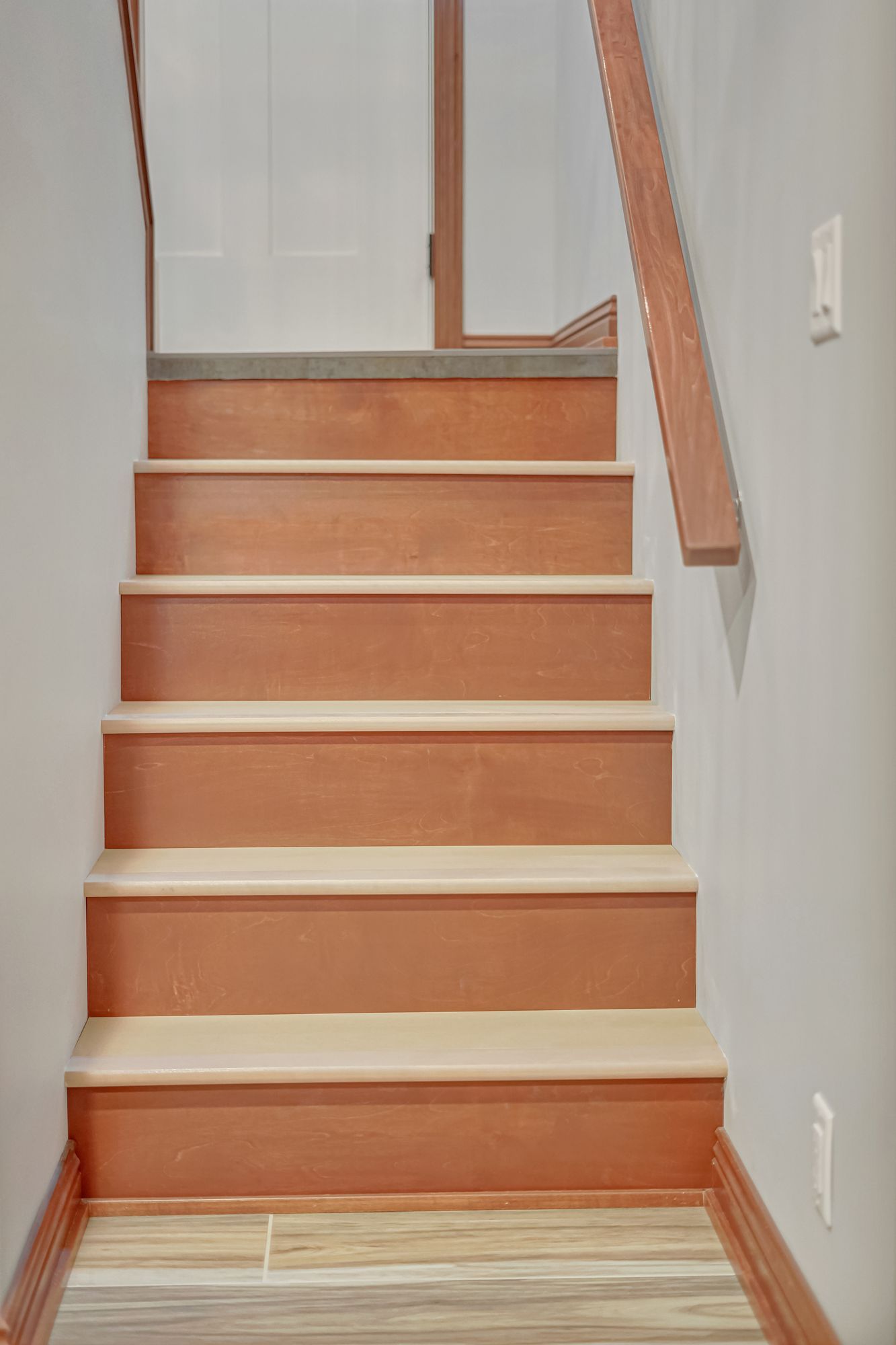 Staircase with brown treads, beige risers, and a wooden handrail. Gray walls.