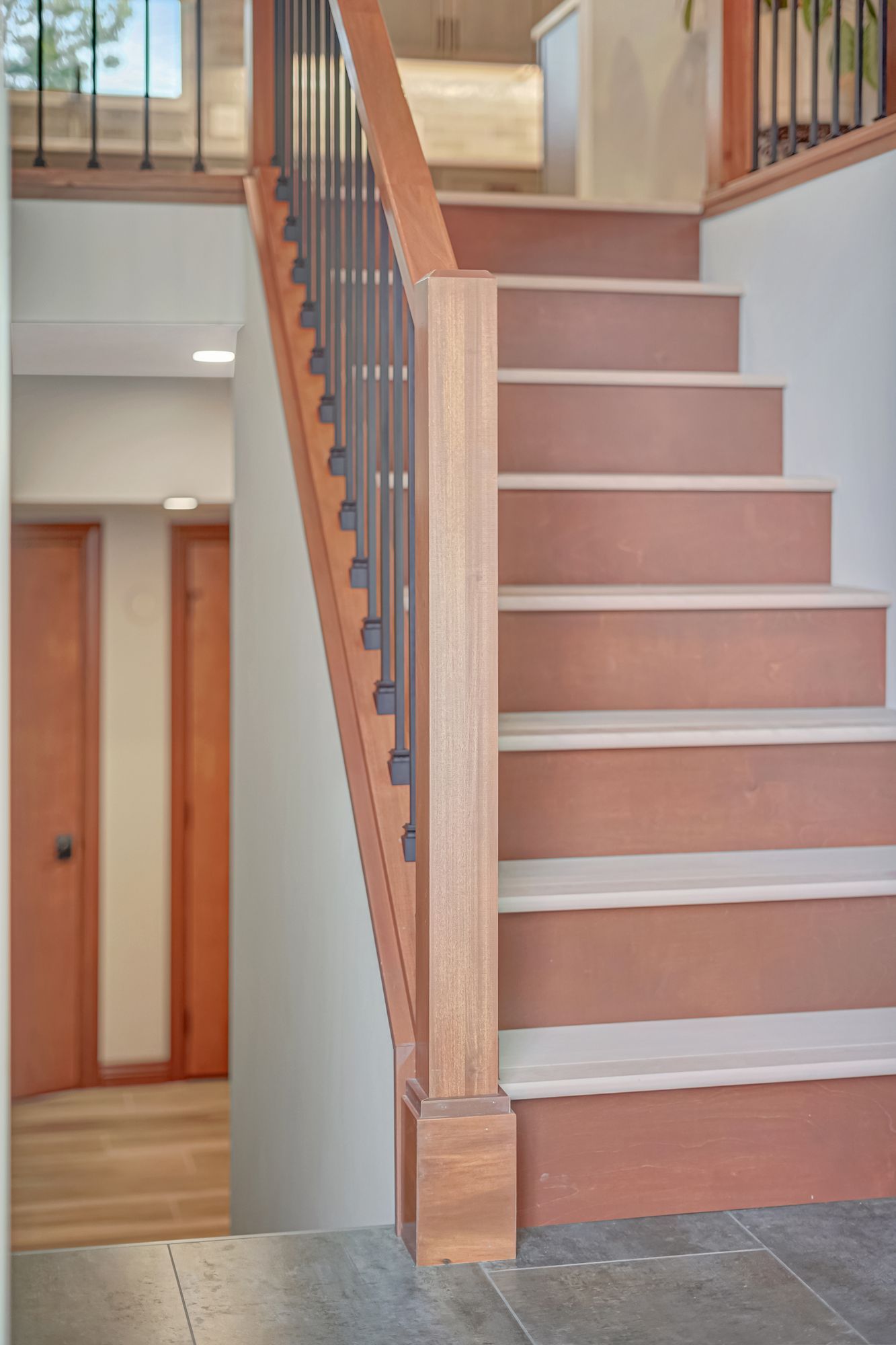 Staircase with reddish-brown treads and white risers, wooden handrail with black vertical spindles.