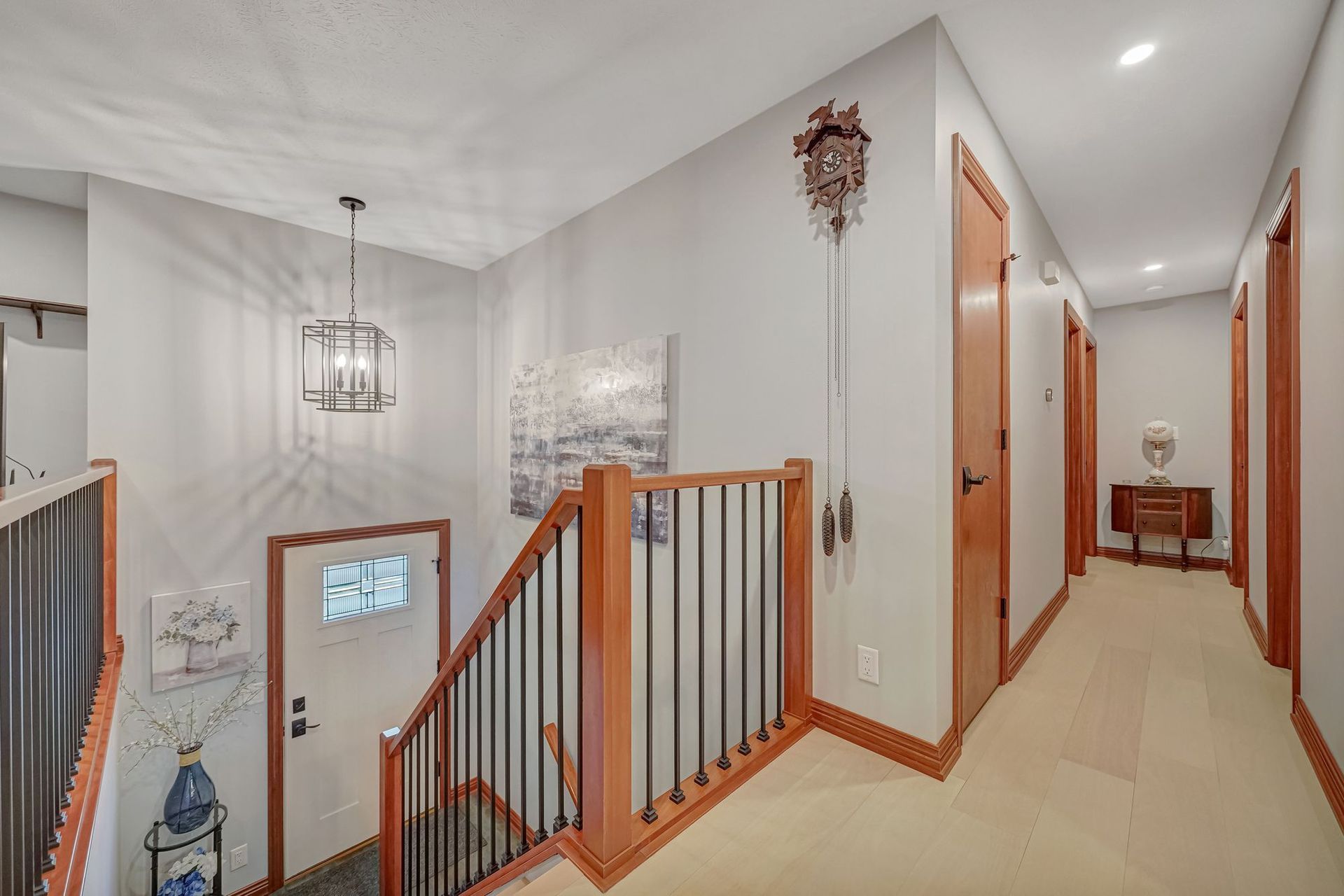 Hallway with stairs, wooden trim, light gray walls, cuckoo clock, and doors.