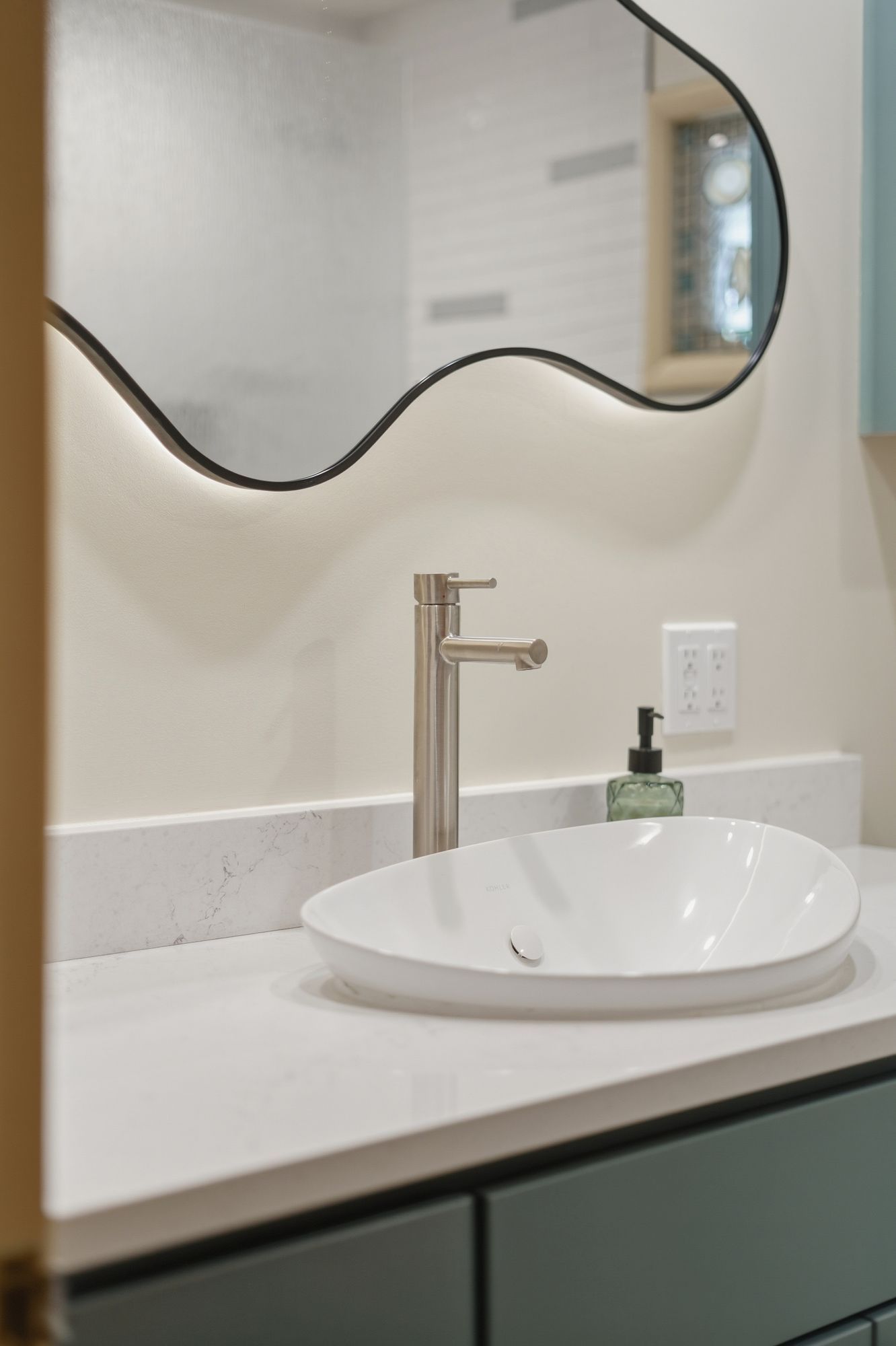 Modern bathroom vanity with oval sink, chrome faucet, and wavy mirror above a white countertop