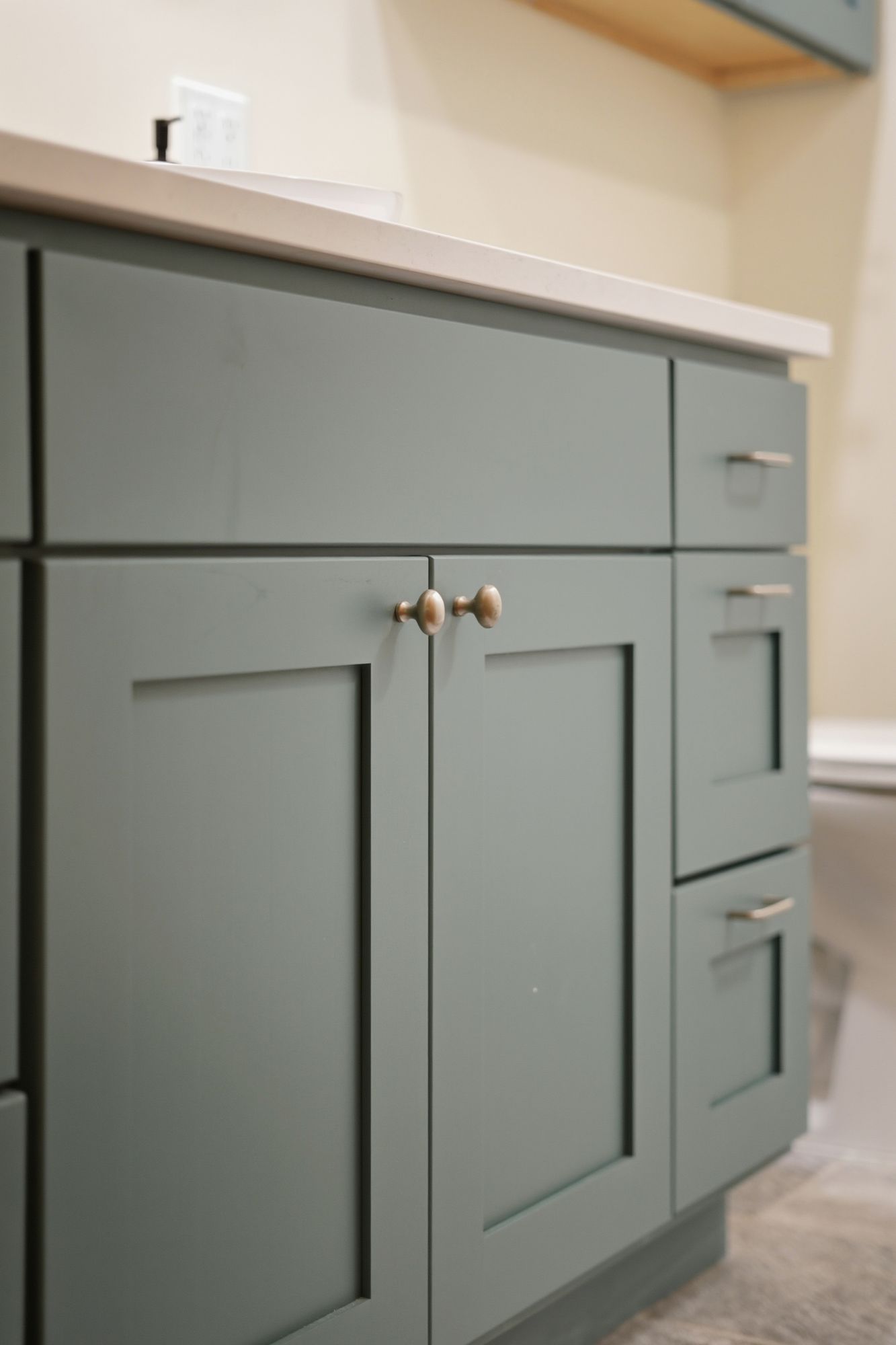 Green bathroom vanity with brass knobs and white countertop under warm light