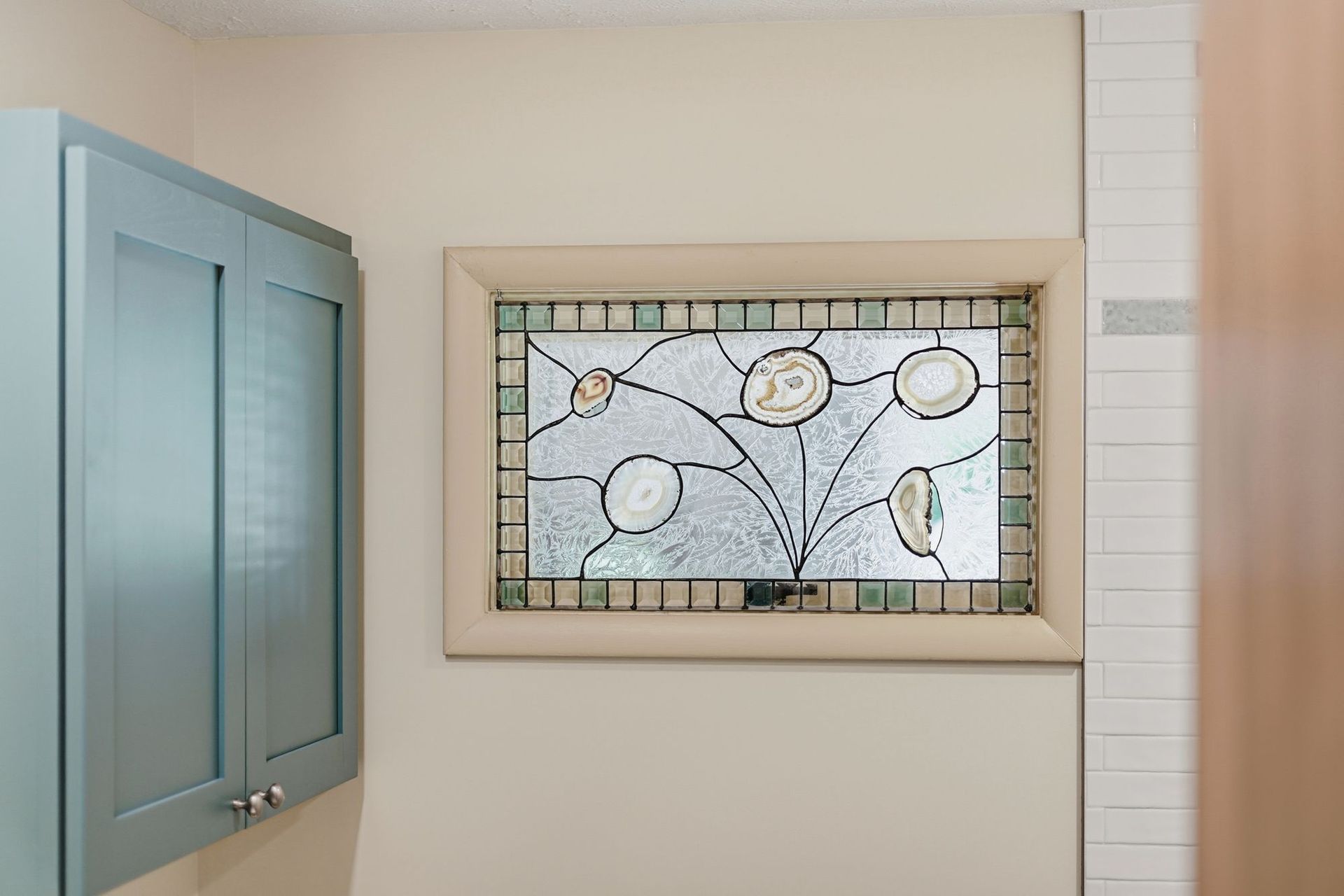 Bathroom wall with blue cabinet and a stained-glass window depicting birds and branches