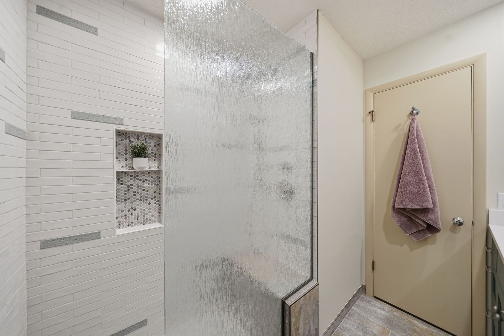 Modern bathroom with tiled shower, glass partition, and a towel hanging on the door