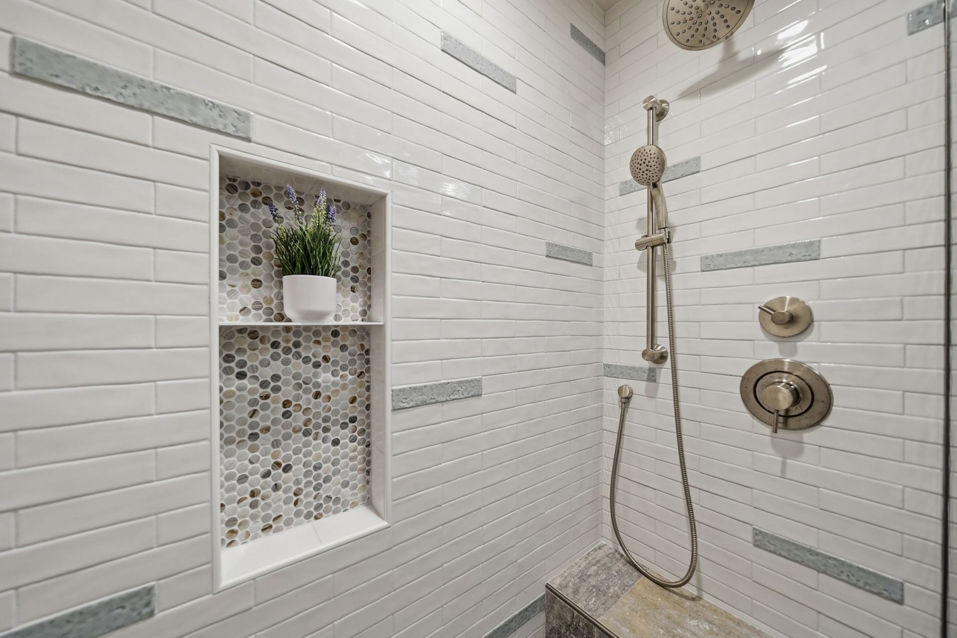 Modern white-tiled shower with built-in shelf, mosaic niche, and brass fixtures