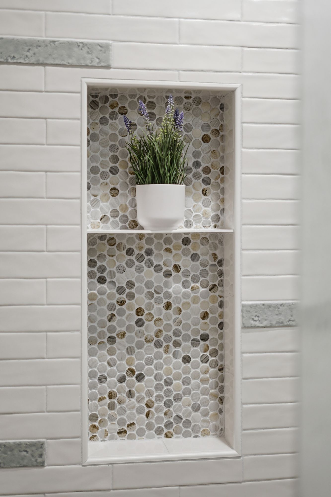 White tiled bathroom niche with mosaic backing, a potted plant, and a small white container on the shelf