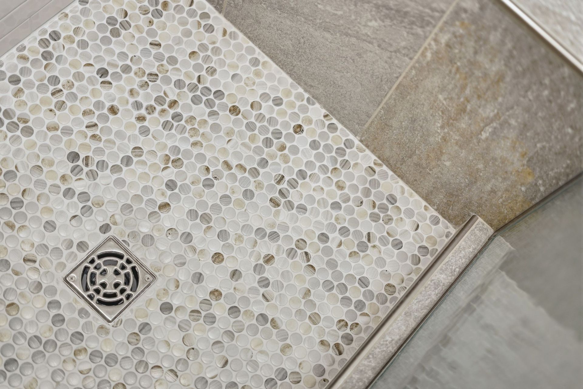Pebble mosaic shower floor with a square drain and gray stone tile edging